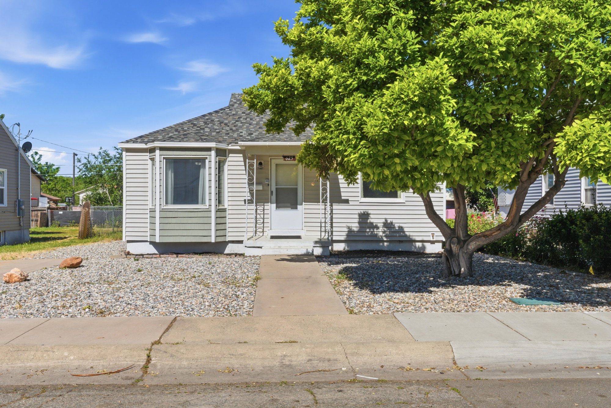 Charming front exterior with updated siding, mature shade tree, rock landscaping, and welcoming covered entry.