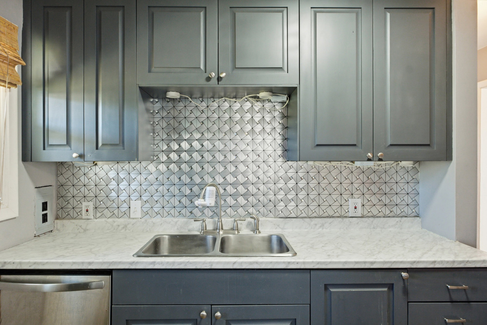 Kitchen area featuring gray shaker-style cabinetry, a stainless steel double basin sink, and a patterned tile backsplash