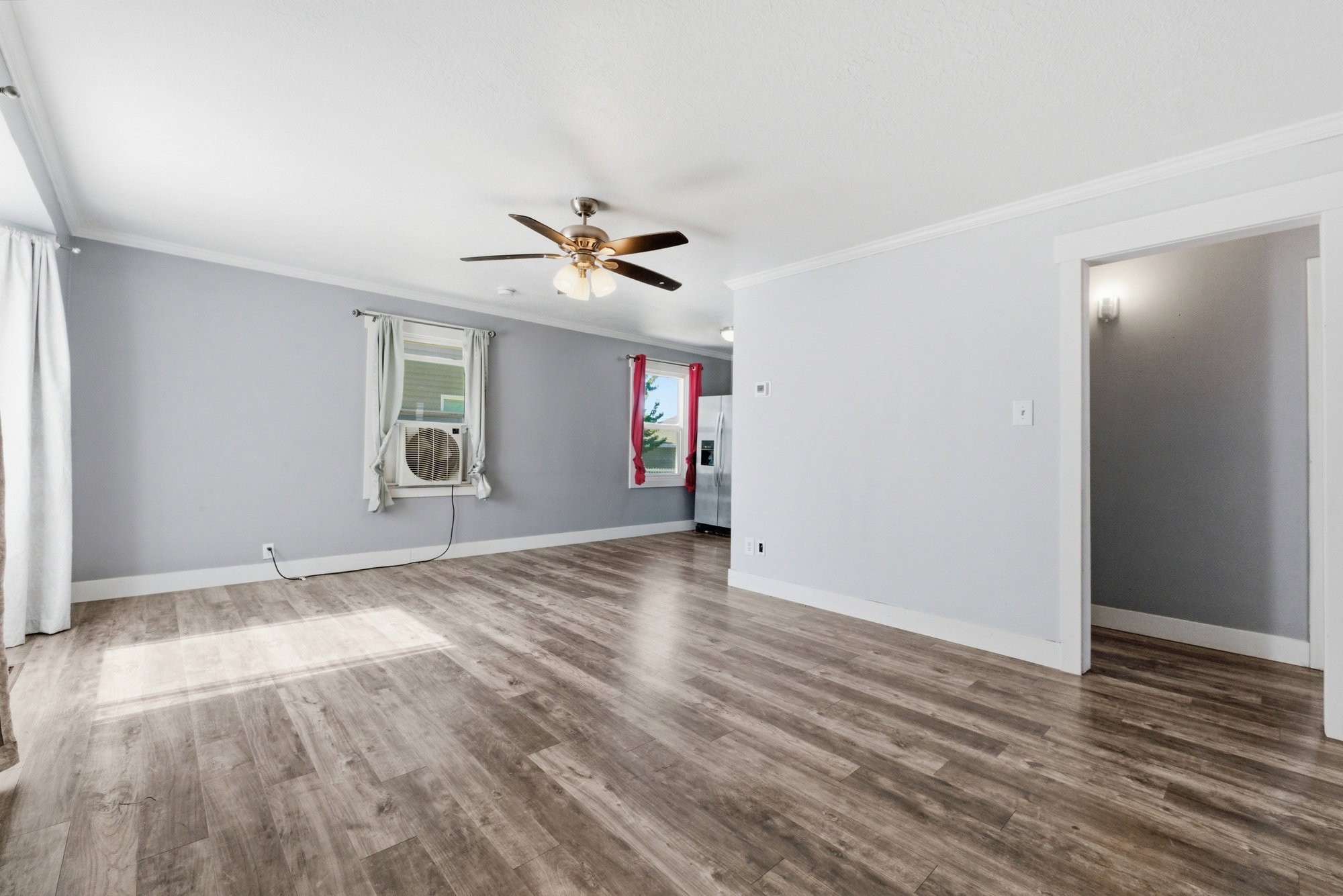Spacious open living area with updated flooring, neutral paint, ceiling fan, and natural light throughout.