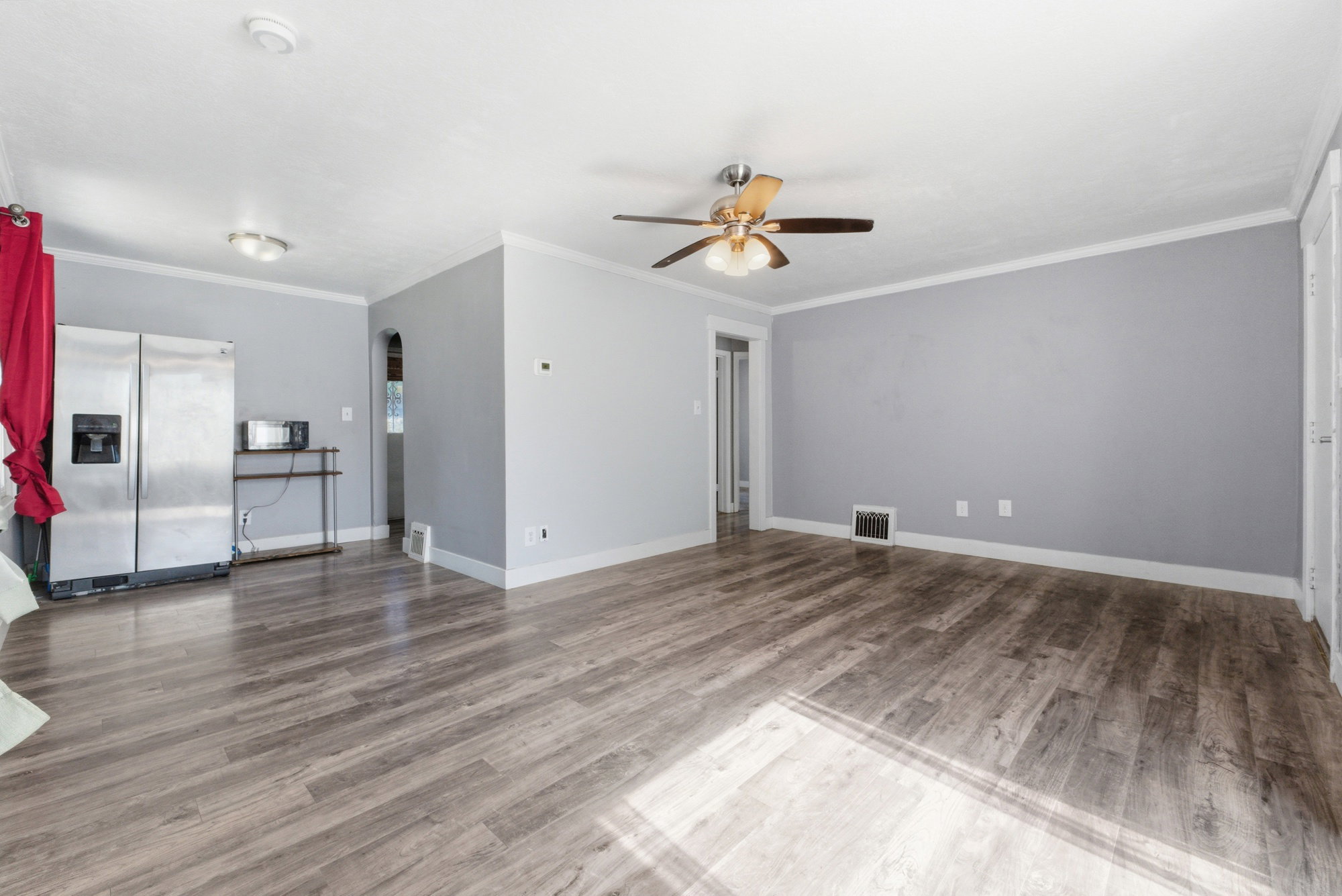 Open main living space with LVP flooring, gray walls, white trim, ceiling fan, and flexible layout.