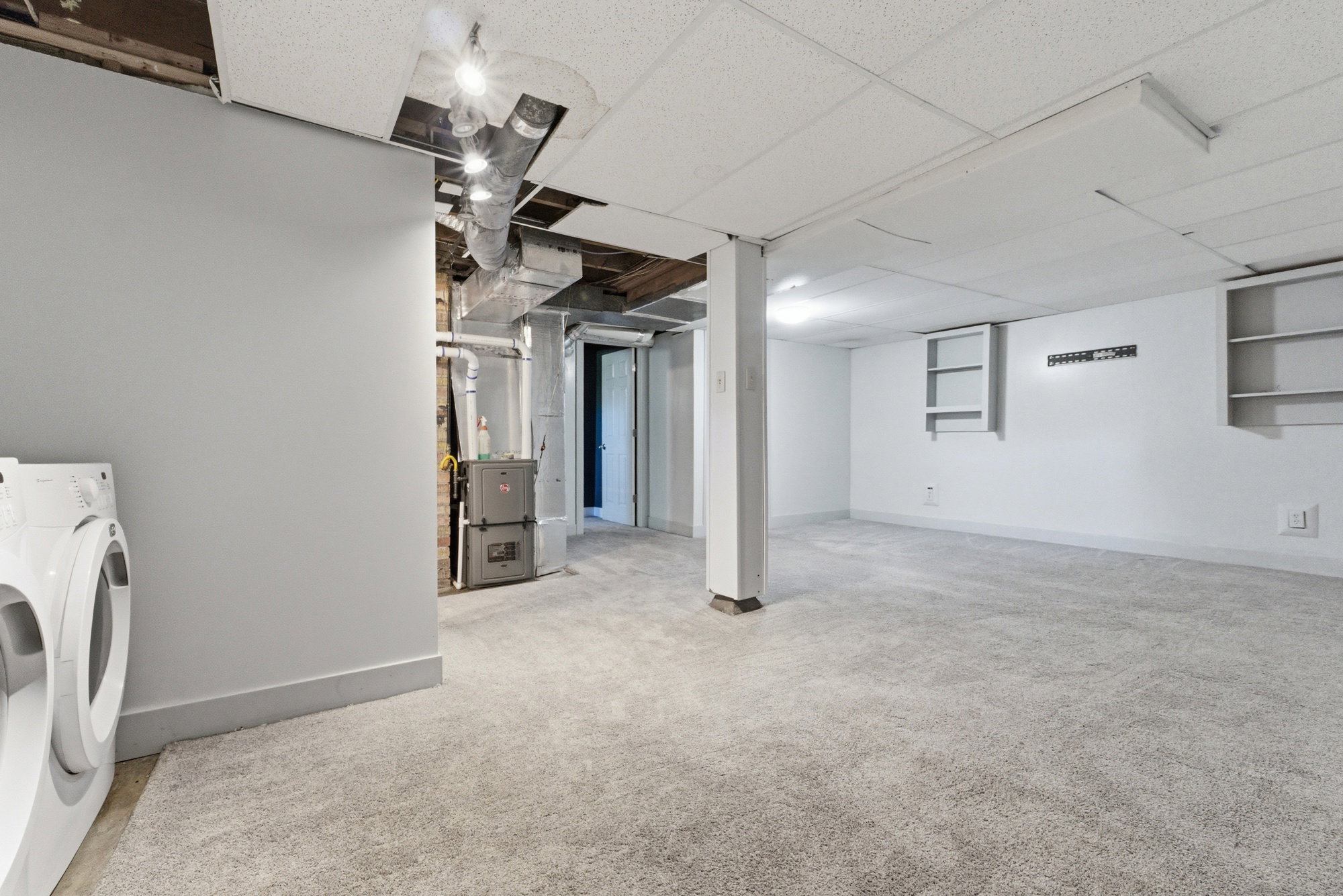 Basement living area with carpet, laundry area nearby, utility access, and flexible open space.