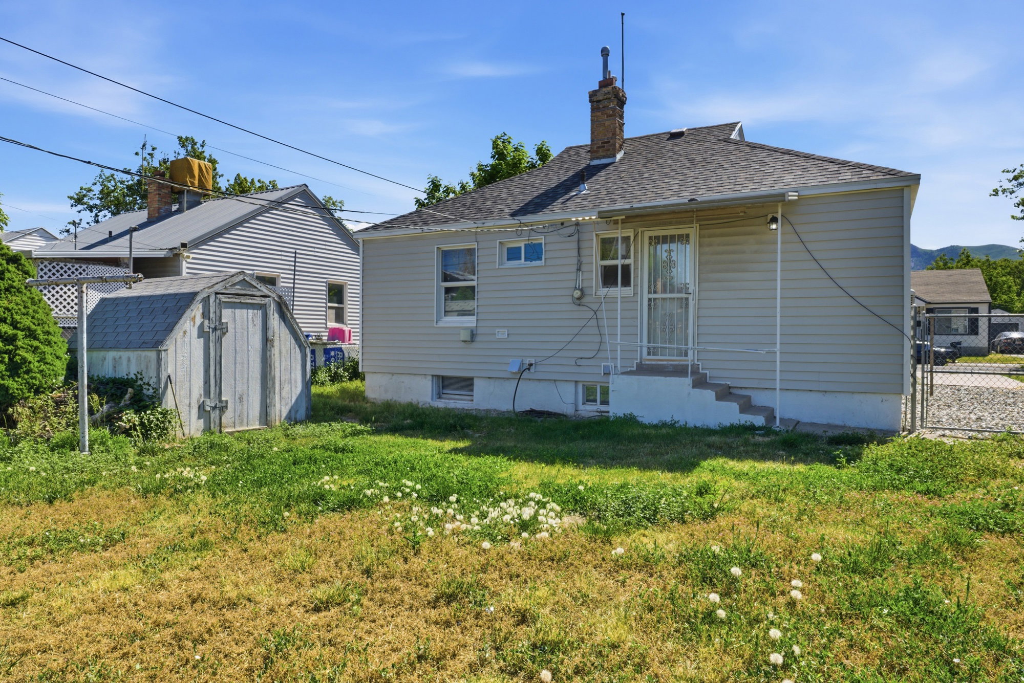 Back exterior view featuring rear entry, basement windows, storage shed, and spacious yard area.