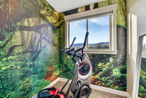 Room featuring vibrant forest-themed wall coverings, a large window, white window trim, and a mountain and sky backdrop