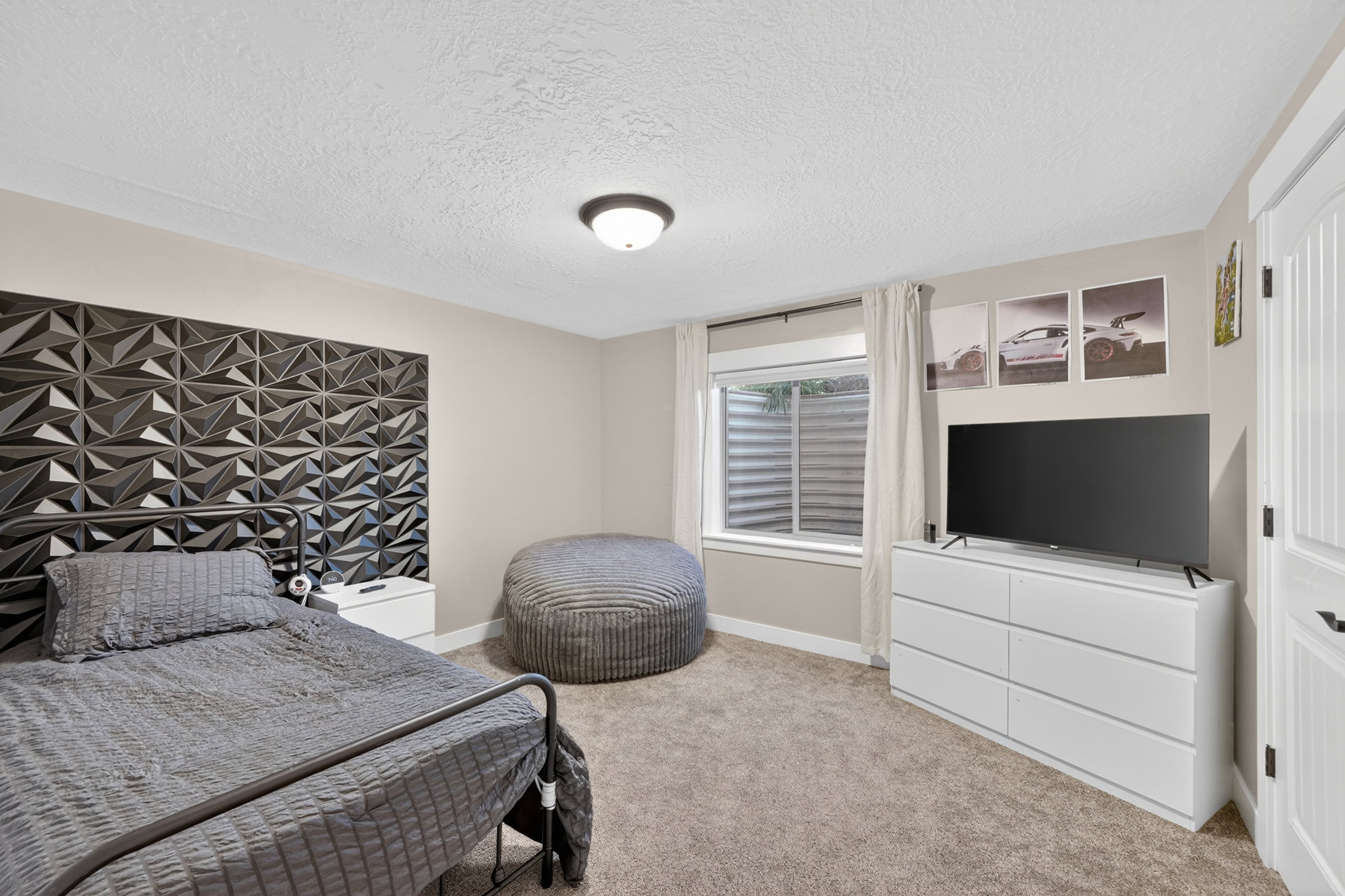 Carpeted bedroom featuring a textured accent wall, a flush-mount ceiling light fixture, a window with a window well, and a paneled interior door
