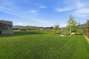 Expansive green lawn with a decorative pond feature, surrounded by mature trees and a wood fence