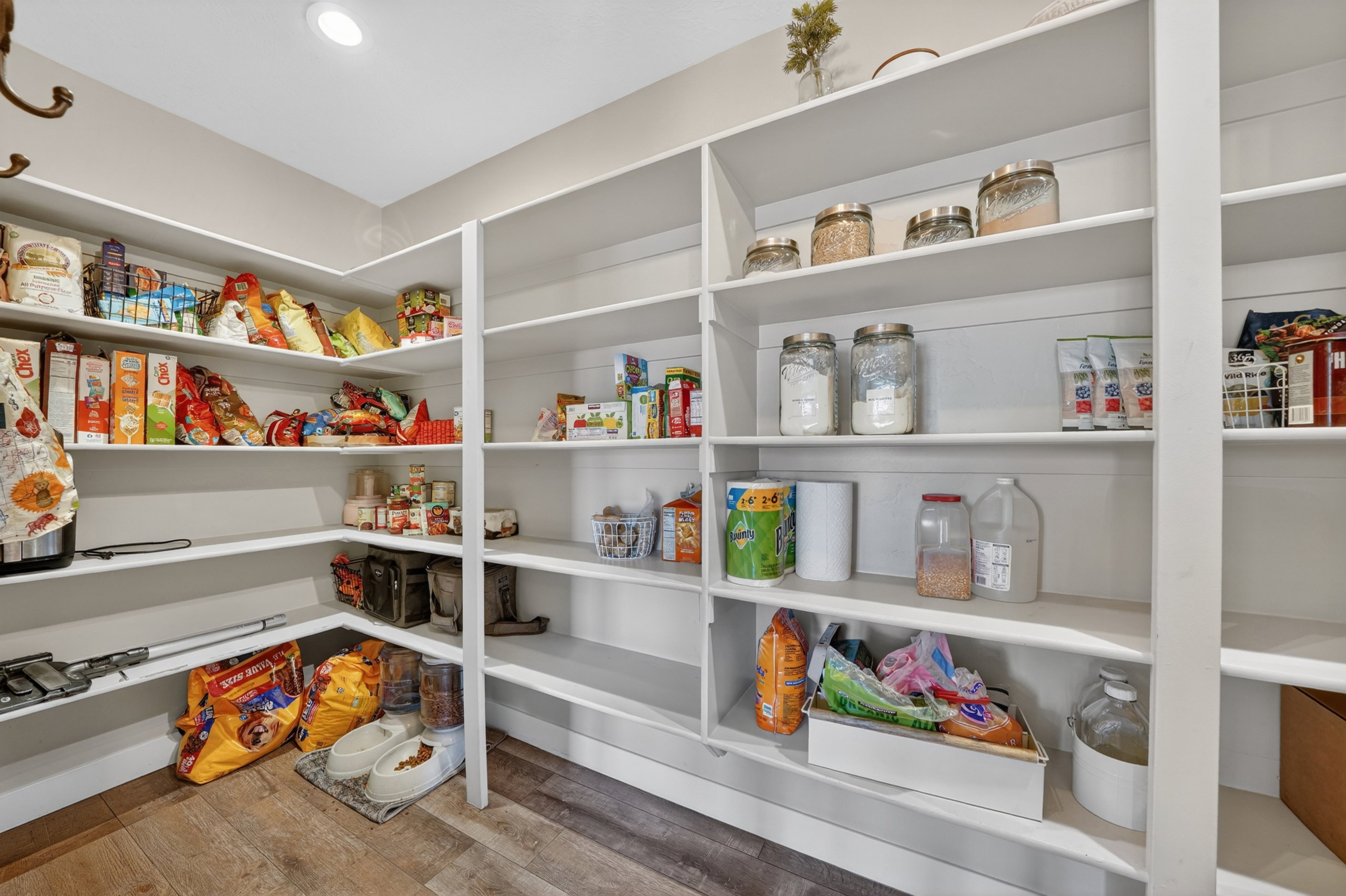 Spacious walk-in pantry featuring extensive white shelving, recessed lighting, and wood-finish flooring
