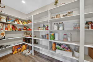 Spacious walk-in pantry featuring extensive white shelving, recessed lighting, and wood-finish flooring