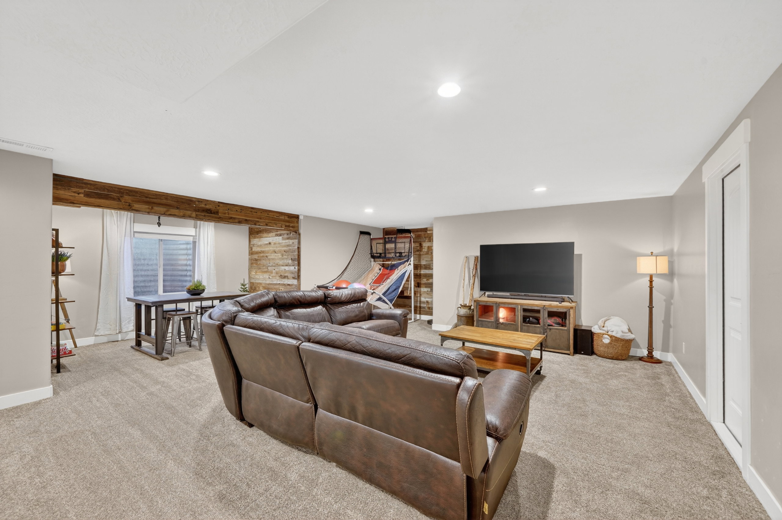 Spacious entertainment room featuring recessed ceiling lighting, light-toned carpet flooring, and a window with horizontal blinds