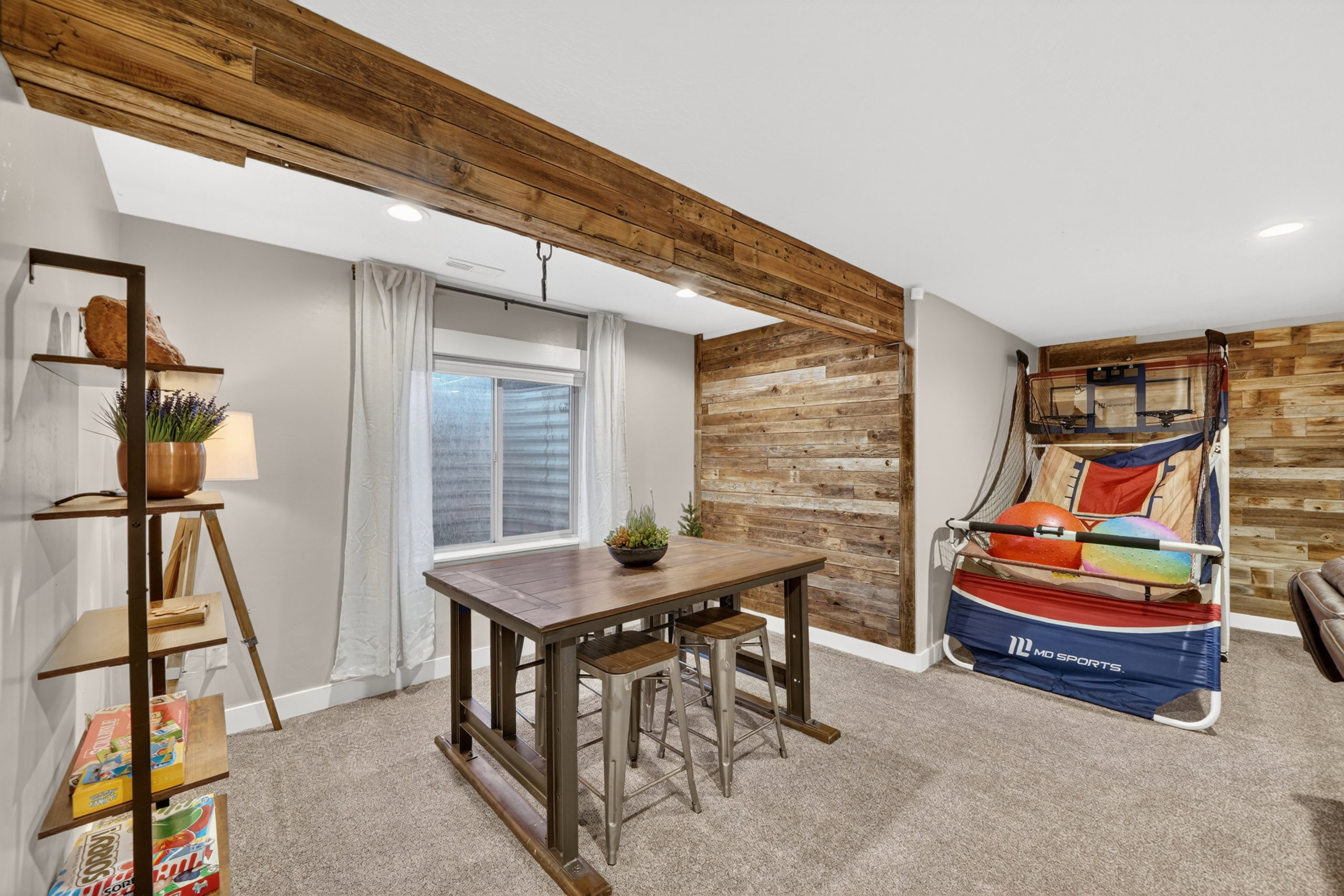 Finished room featuring a wood-finish accent wall, exposed wood-finish beam, recessed lighting, window with privacy screen, and carpeted flooring