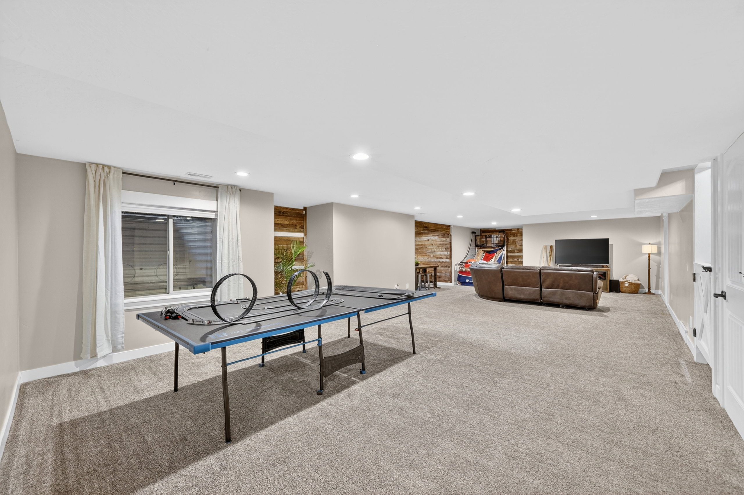 Spacious carpeted room featuring recessed lighting, a window with blinds, and an accent wall with horizontal wood paneling