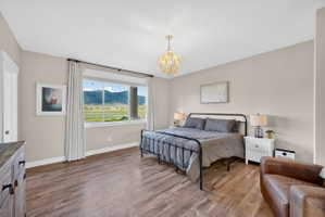 Bedroom featuring wood-finish flooring, a contemporary chandelier, neutral wall tones, and a large picture window