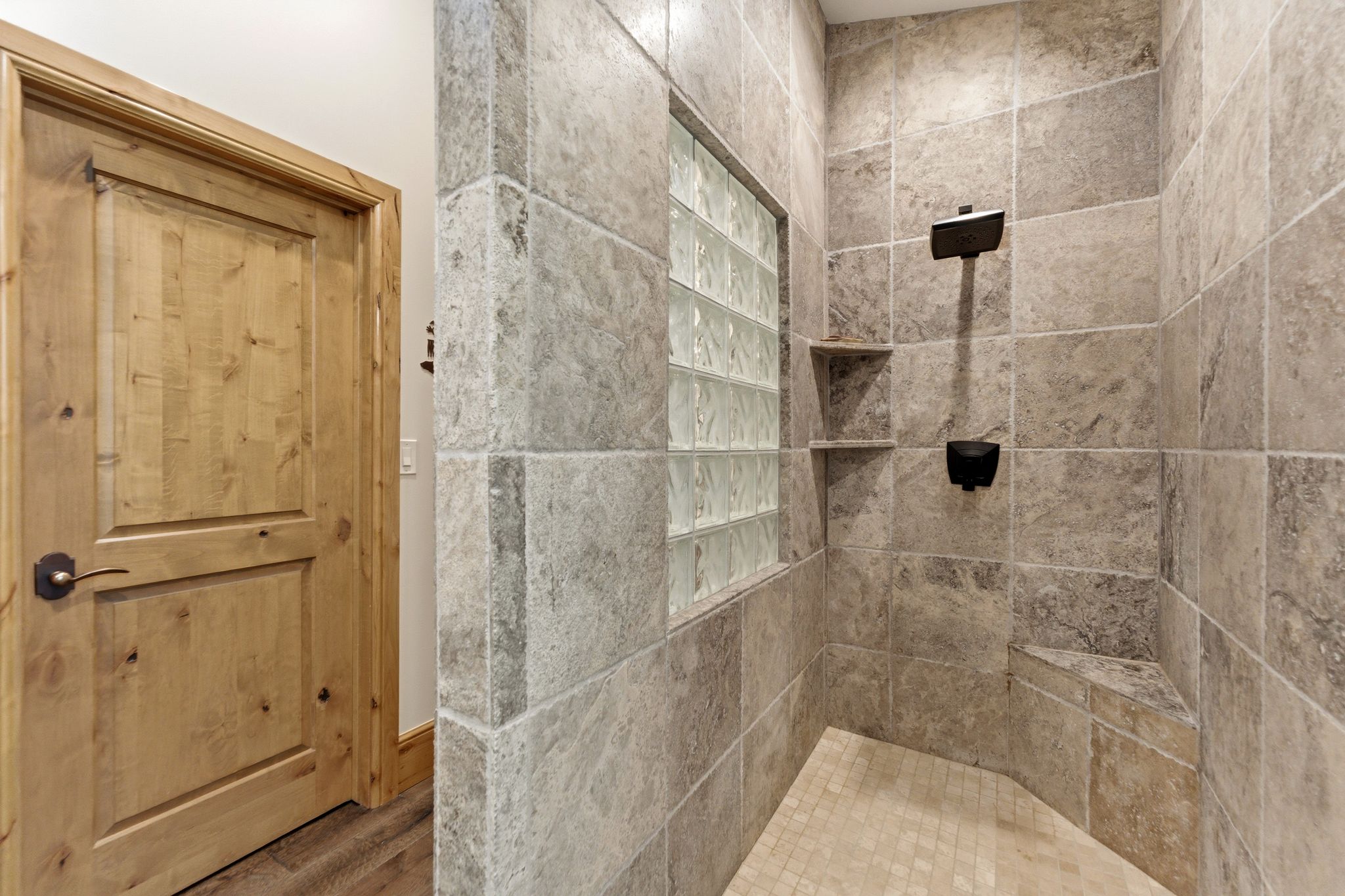 Spacious walk-in shower featuring large format tile walls, a built-in bench, and a glass block window