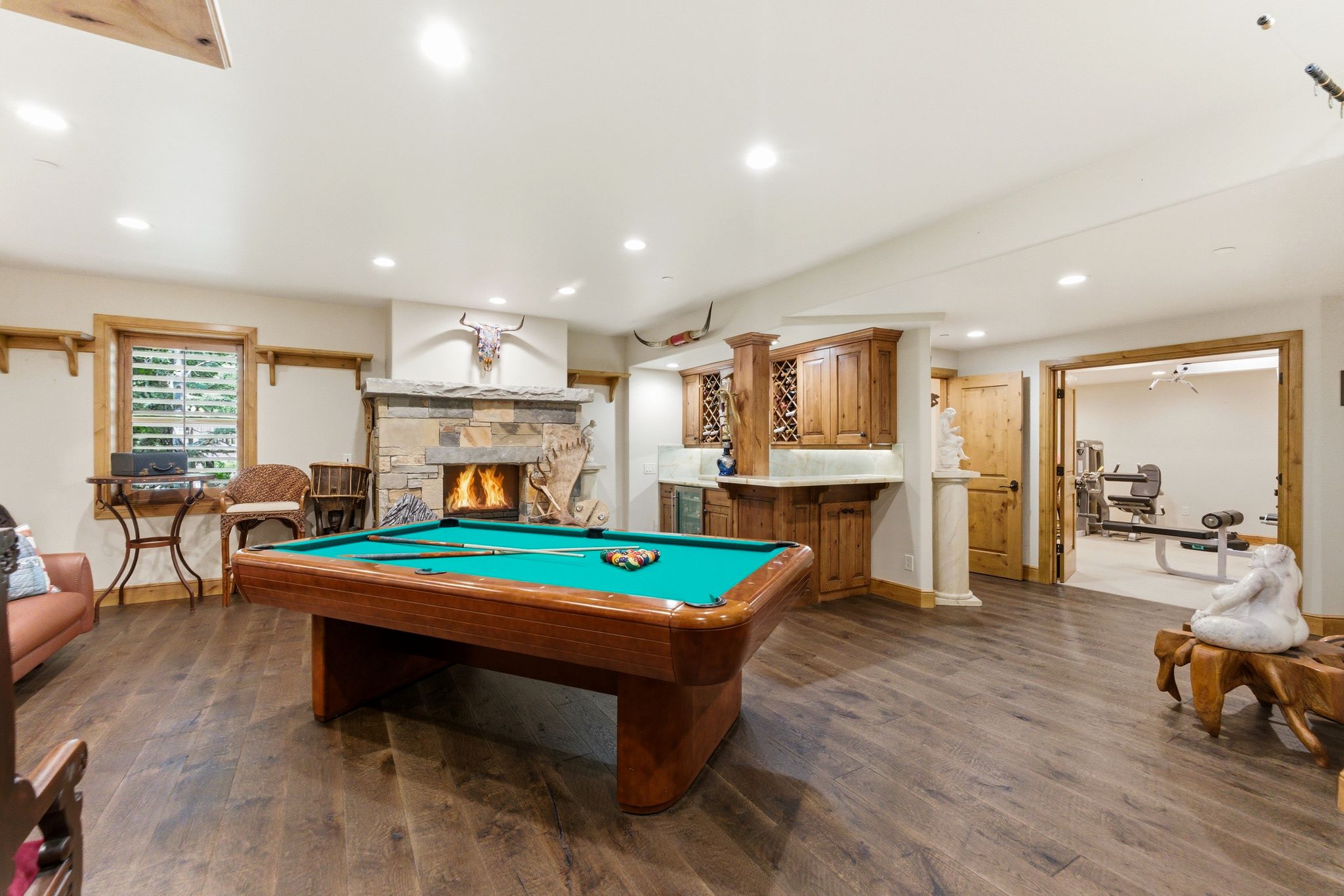 Spacious recreation room featuring wood-finish flooring, a stone fireplace, and a built-in wet bar with cabinetry
