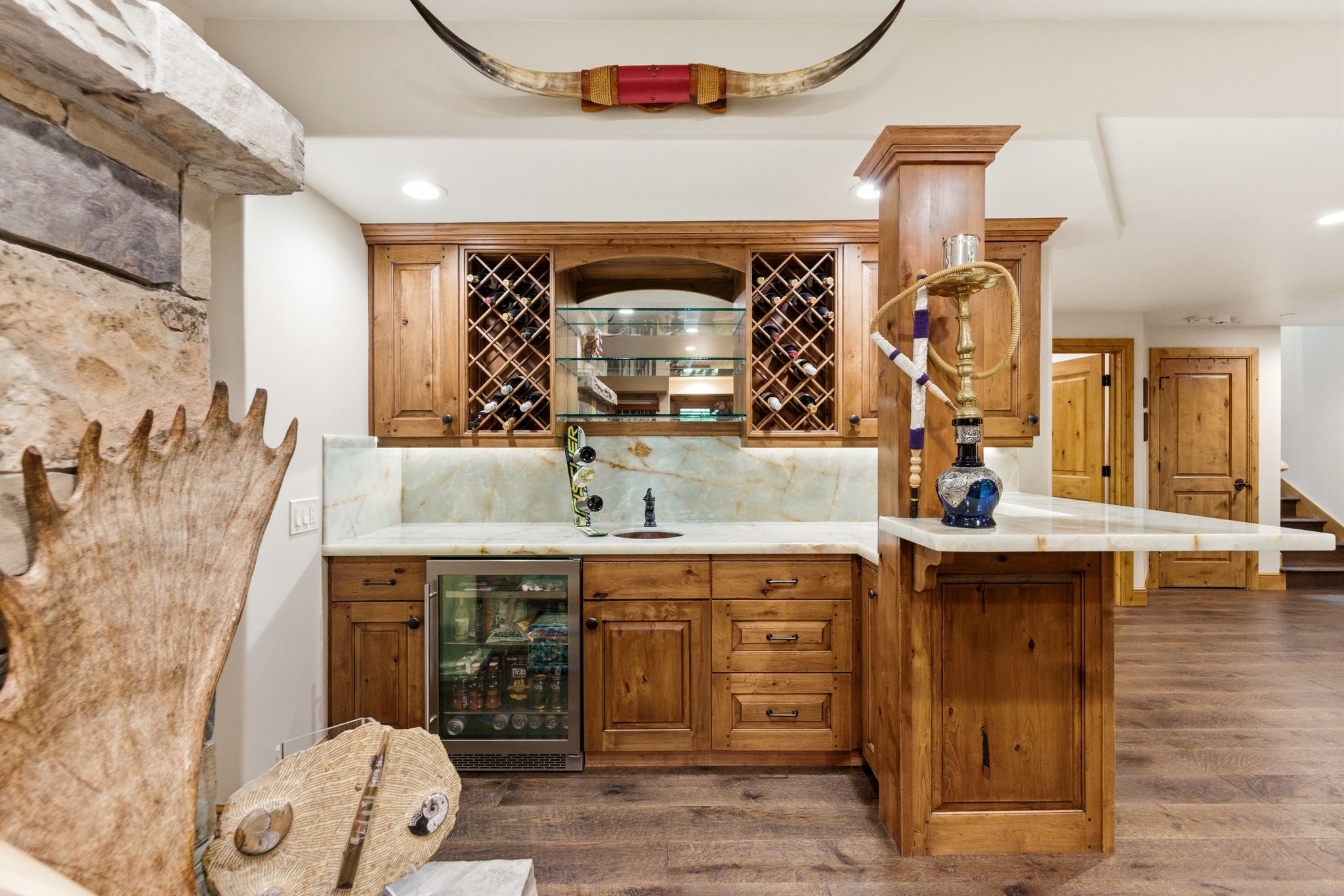 Custom wet bar featuring wood cabinetry, integrated wine storage, under-cabinet lighting, a beverage refrigerator, and stone countertops with a matching backsplash