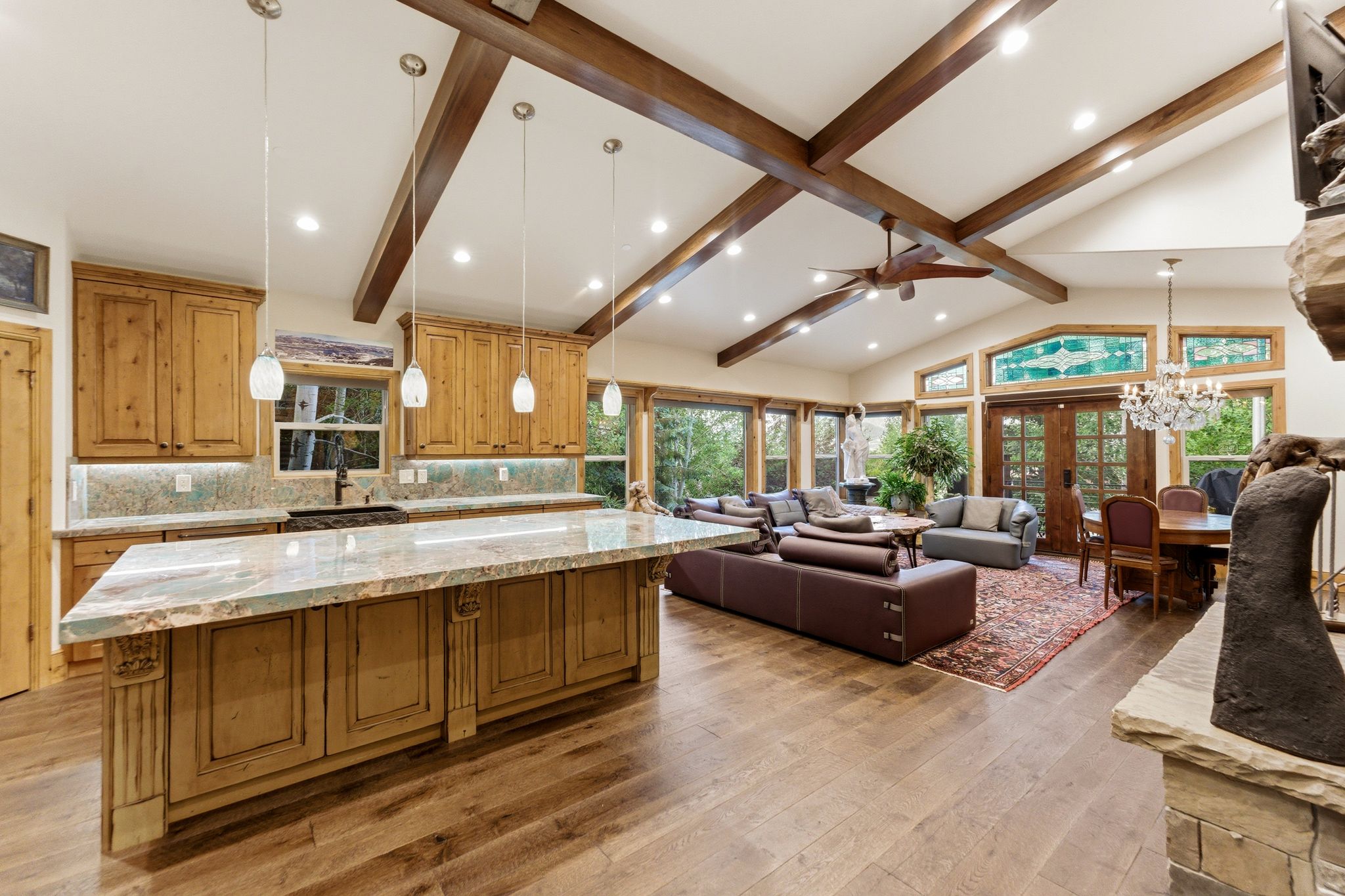 Open-concept living area featuring a vaulted ceiling with exposed wood beams, hardwood flooring, and a stone fireplace