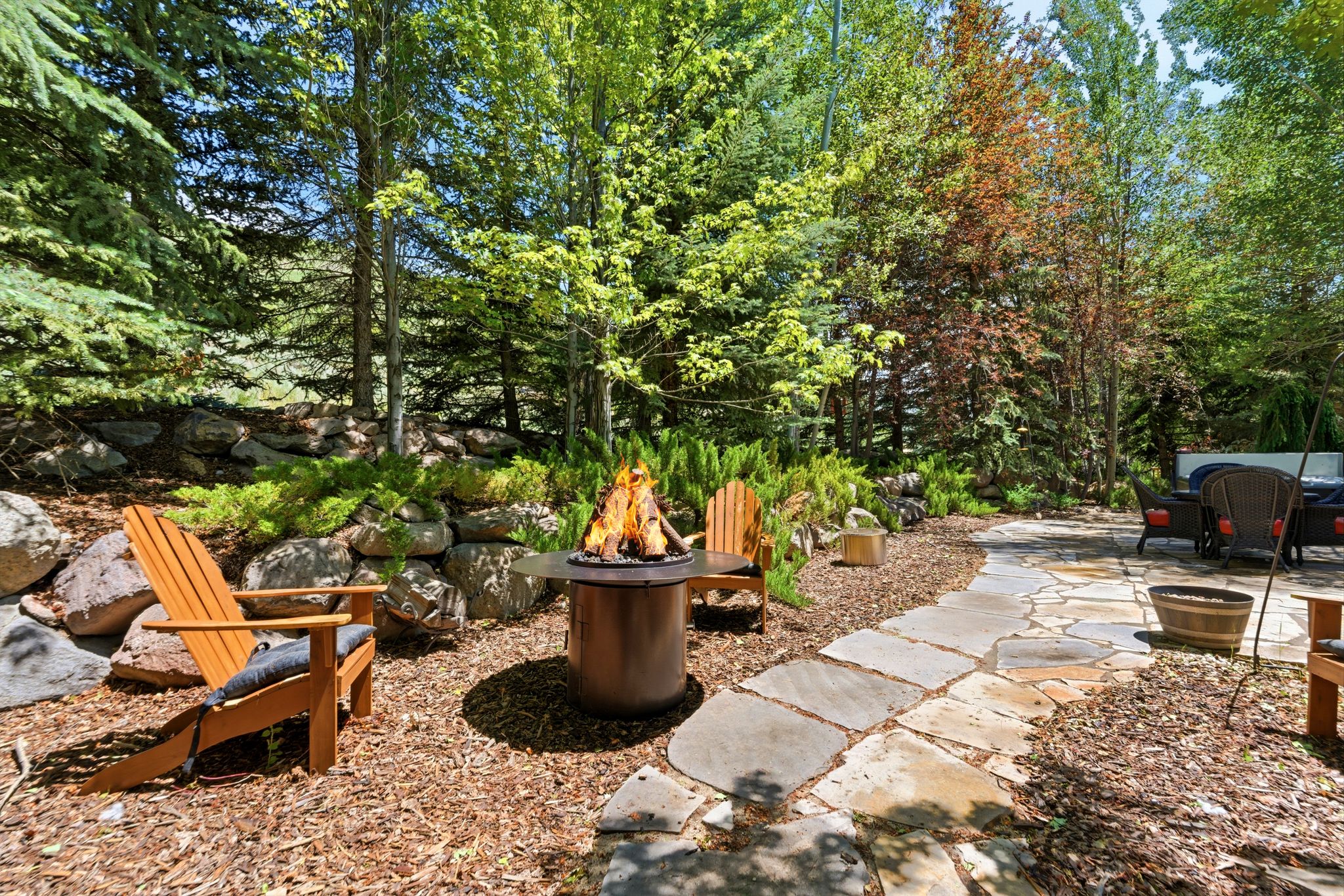 Outdoor fire pit area featuring a stone retaining wall and surrounding mature trees