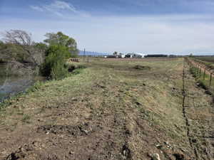 Expansive land parcel featuring a water source, established perimeter fencing, and distant agricultural structures under a clear sky