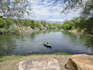 Waterfront property featuring a tranquil river, lush green foliage on the banks, and distant snow-capped mountains under a partially cloudy sky