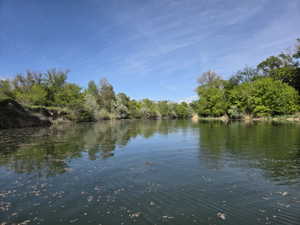 Waterfront property featuring serene water, natural shoreline, mature trees, and open sky