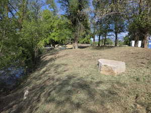 Expansive outdoor area featuring a water feature, mature trees, natural rock elements, and a sloped, grassed terrain