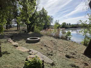 Expansive natural landscape featuring a waterfront, mature trees, a stone pathway, and a built-in fire pit