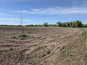 Expansive cleared land featuring rich soil, distant green foliage, and a perimeter fence line