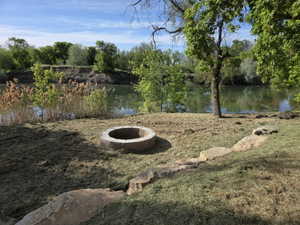 Riverside property featuring a stone fire pit, natural stone accents, mature trees, and a grassy expanse bordering the water