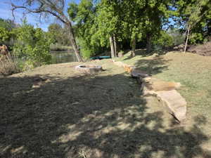 Waterside property featuring a stone fire pit, extensive lawn area, mature trees, and a natural stone retaining wall