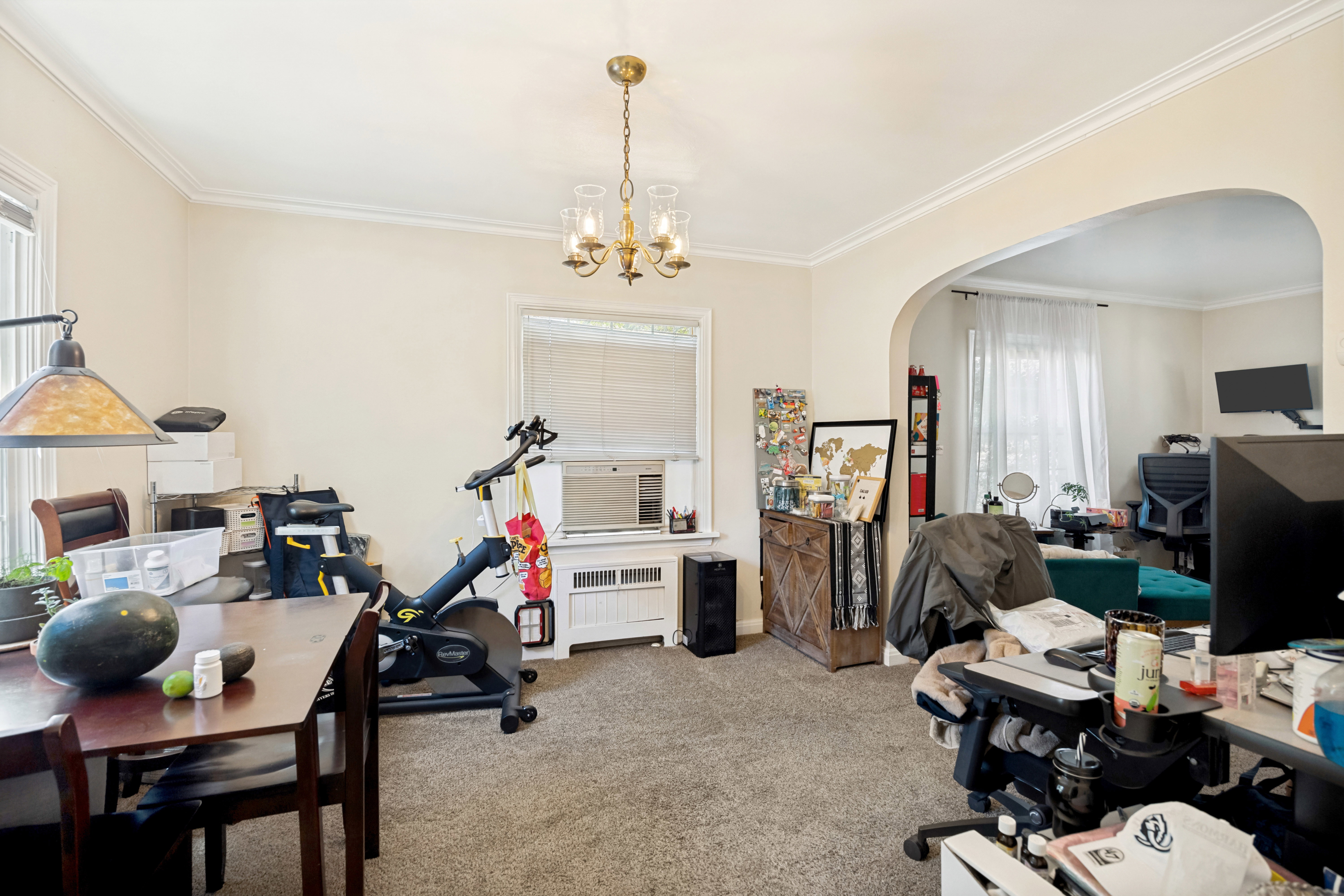 Unit 1 Carpeted interior space featuring a brass chandelier light fixture, crown molding, and an arched doorway