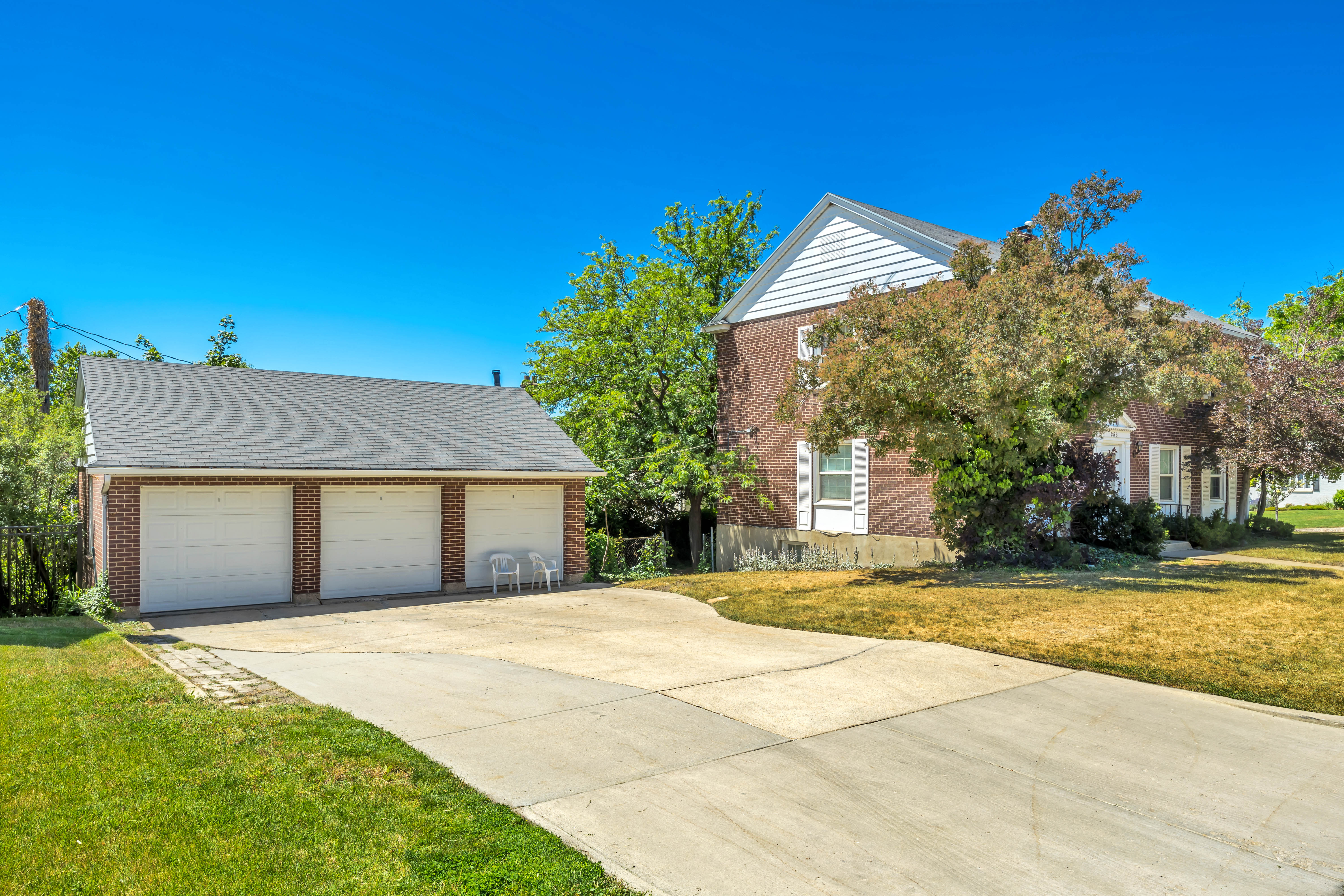 Expansive concrete driveway leading to a three-car detached garage with white paneled doors