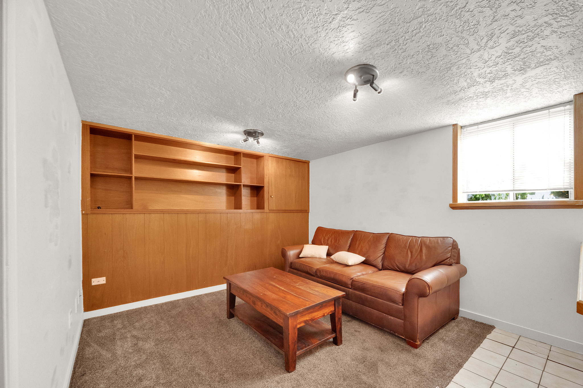Built-in wood shelving and paneling characterize this room, featuring recessed ceiling lights and a window with blinds