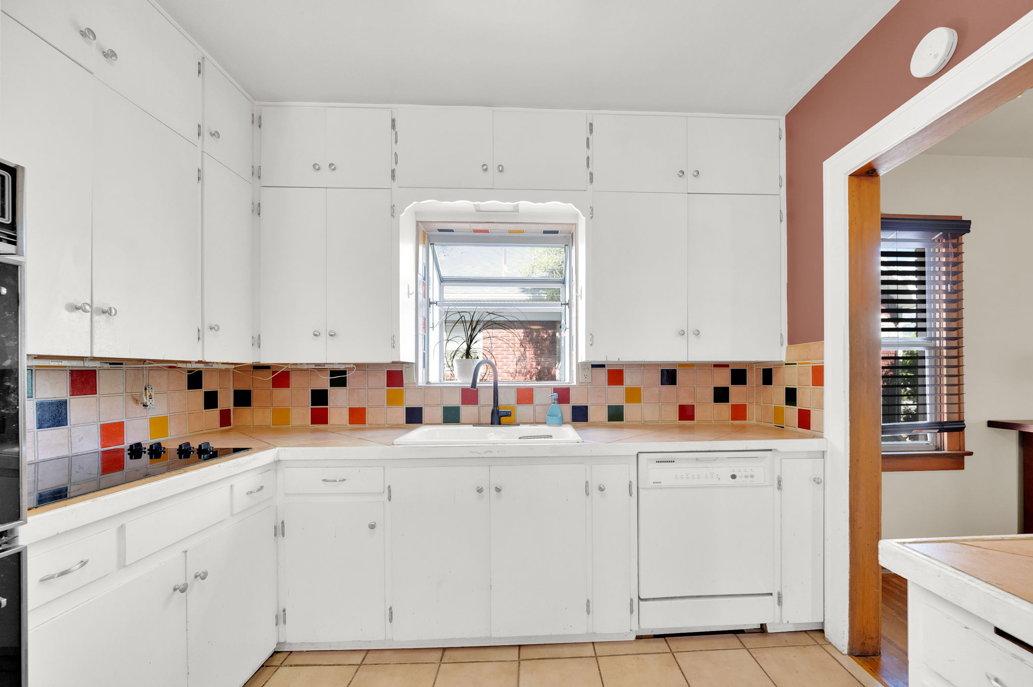 Kitchen featuring white cabinetry, a colorful tiled backsplash, and an integrated cooktop