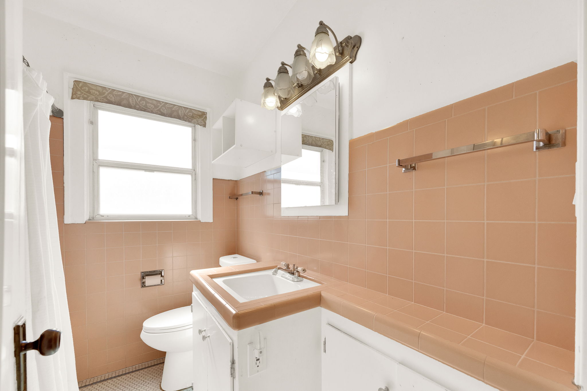 Bathroom featuring peach-toned tile walls, a white vanity with an integrated sink and wood-finish countertop, and a window with a patterned valance