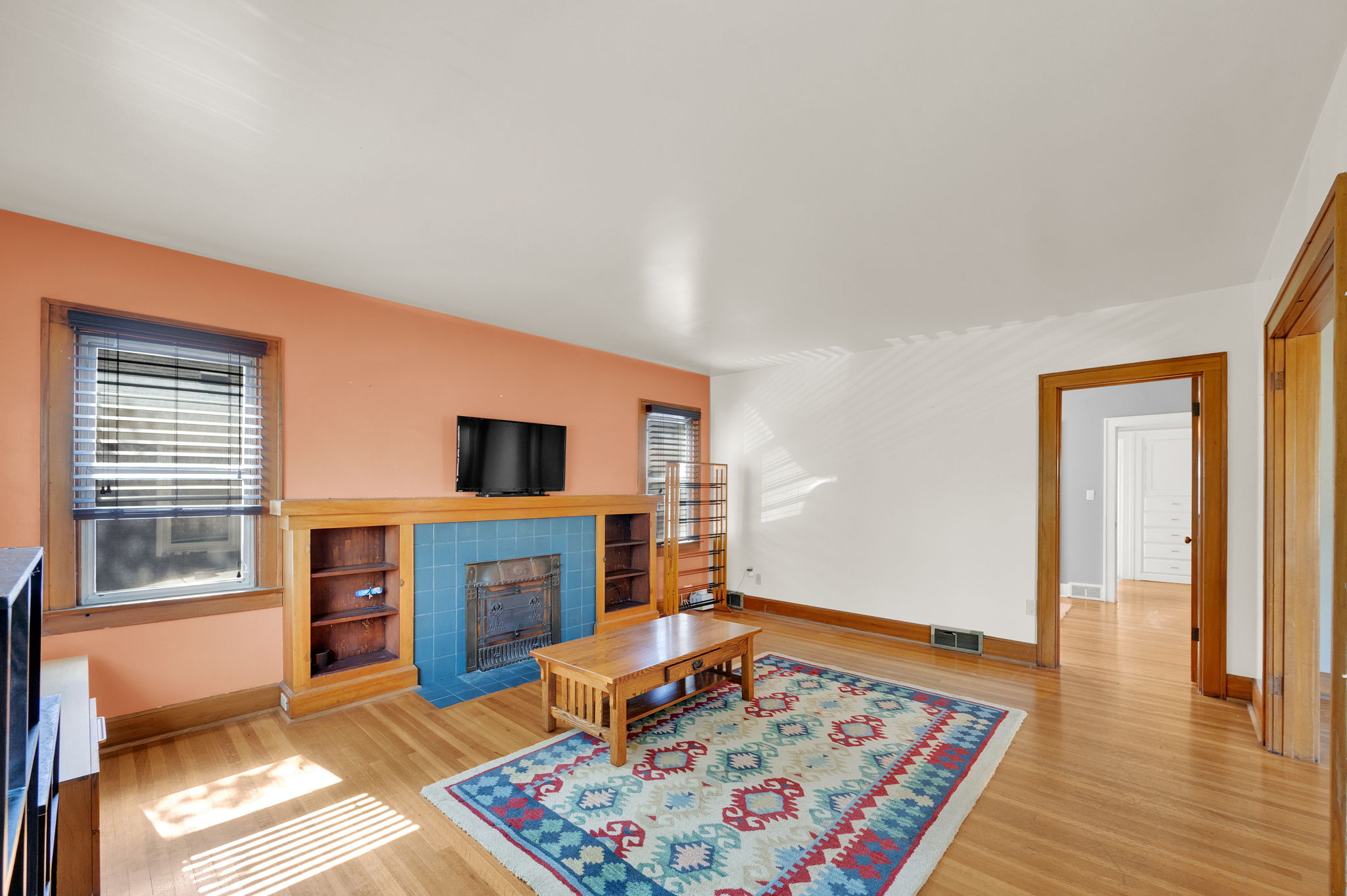 Living area featuring hardwood flooring, a fireplace with blue tile surround, built-in shelving, and wood trim detailing