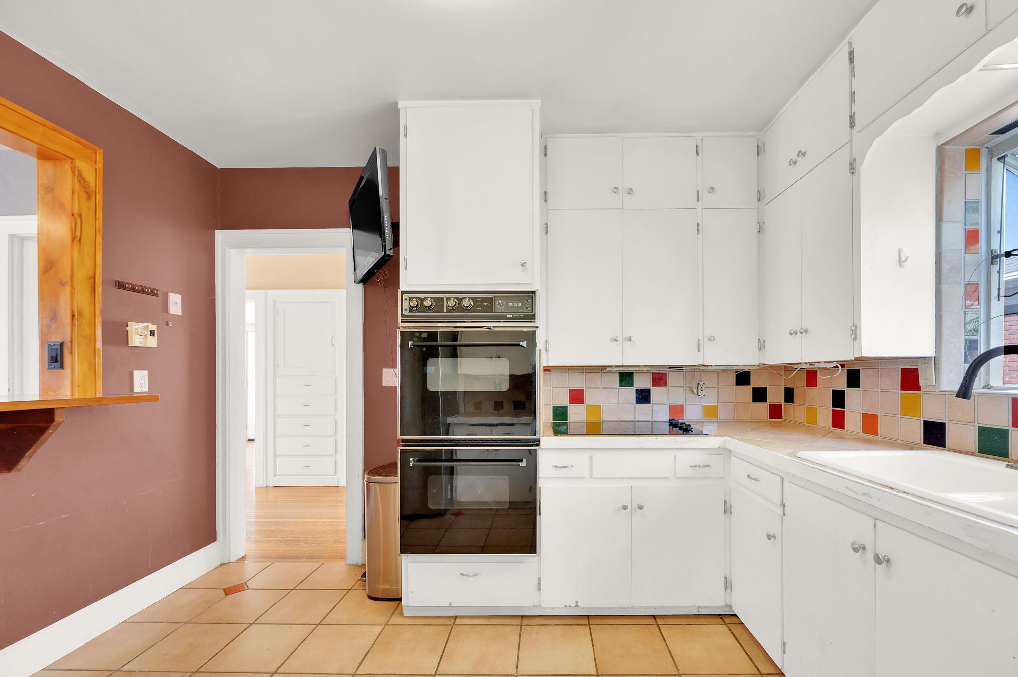 Kitchen featuring white cabinetry, built-in double ovens, a colorful tiled backsplash, and light-toned tile flooring
