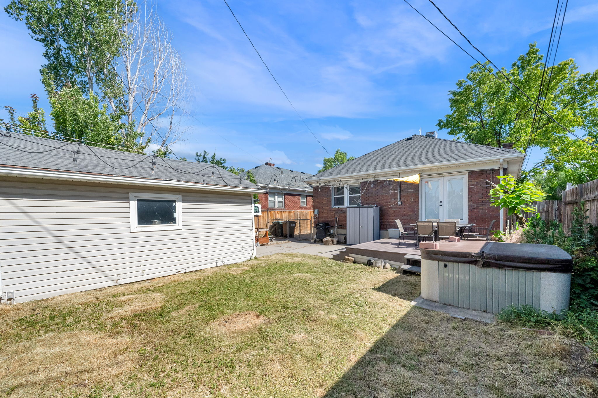 Backyard featuring a wood-finish deck with a built-in spa, a detached outbuilding with horizontal siding, a brick exterior on the main residence, and privacy fencing