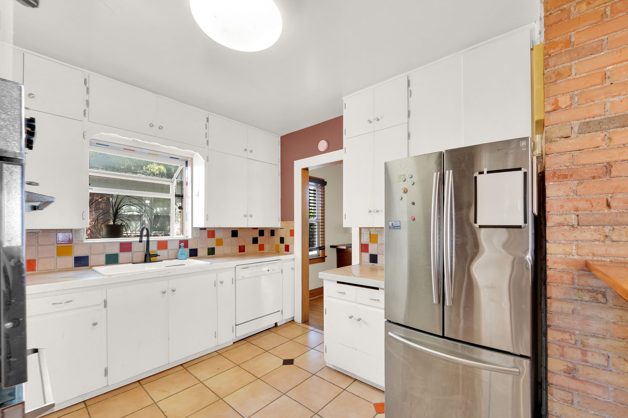 Kitchen featuring white cabinetry, a built-in white sink, a stainless steel refrigerator, and a colorful tile backsplash