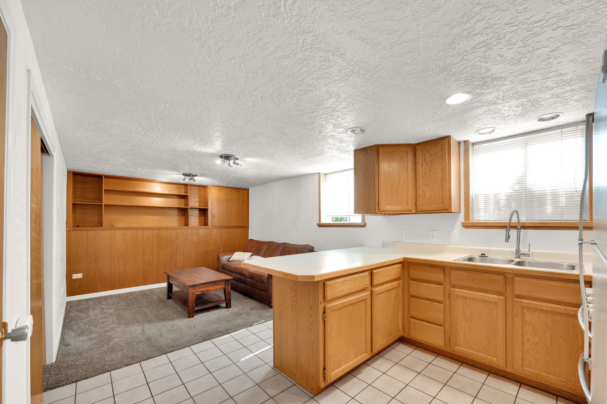 Functional kitchenette featuring light wood cabinetry, a double basin sink, and ample countertop space