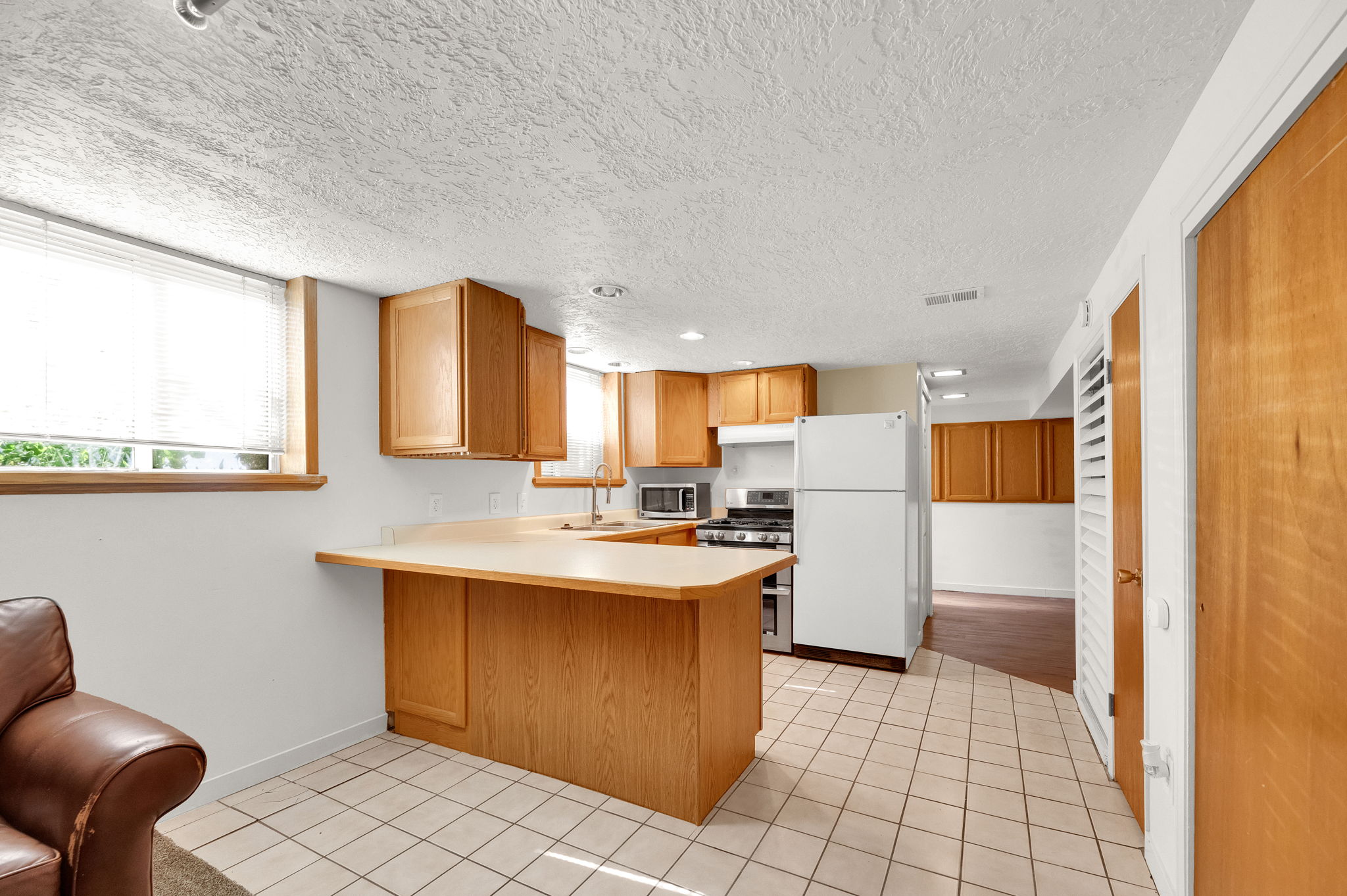 Kitchenette featuring light wood cabinetry, a light-toned countertop with an integrated breakfast bar, white tile flooring, and a stainless steel gas range