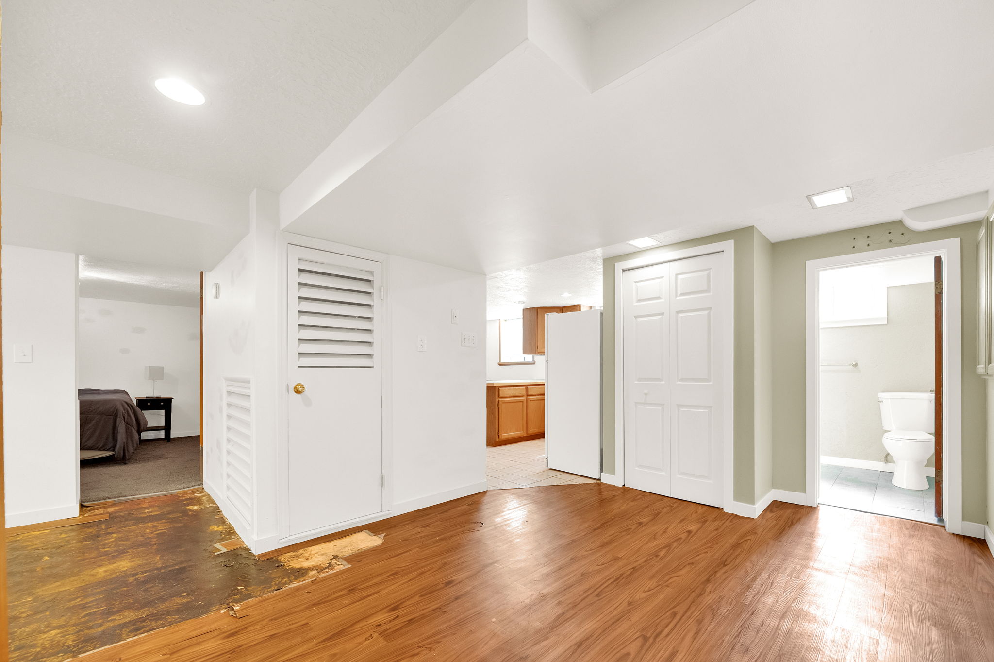 Wood-finish flooring throughout the main area, with a full-size refrigerator and wood cabinetry visible