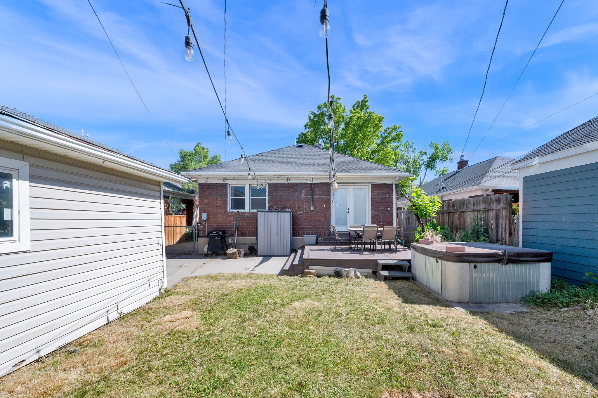 Backyard featuring a wood deck patio, brick exterior, vinyl siding on the garage, and string lighting