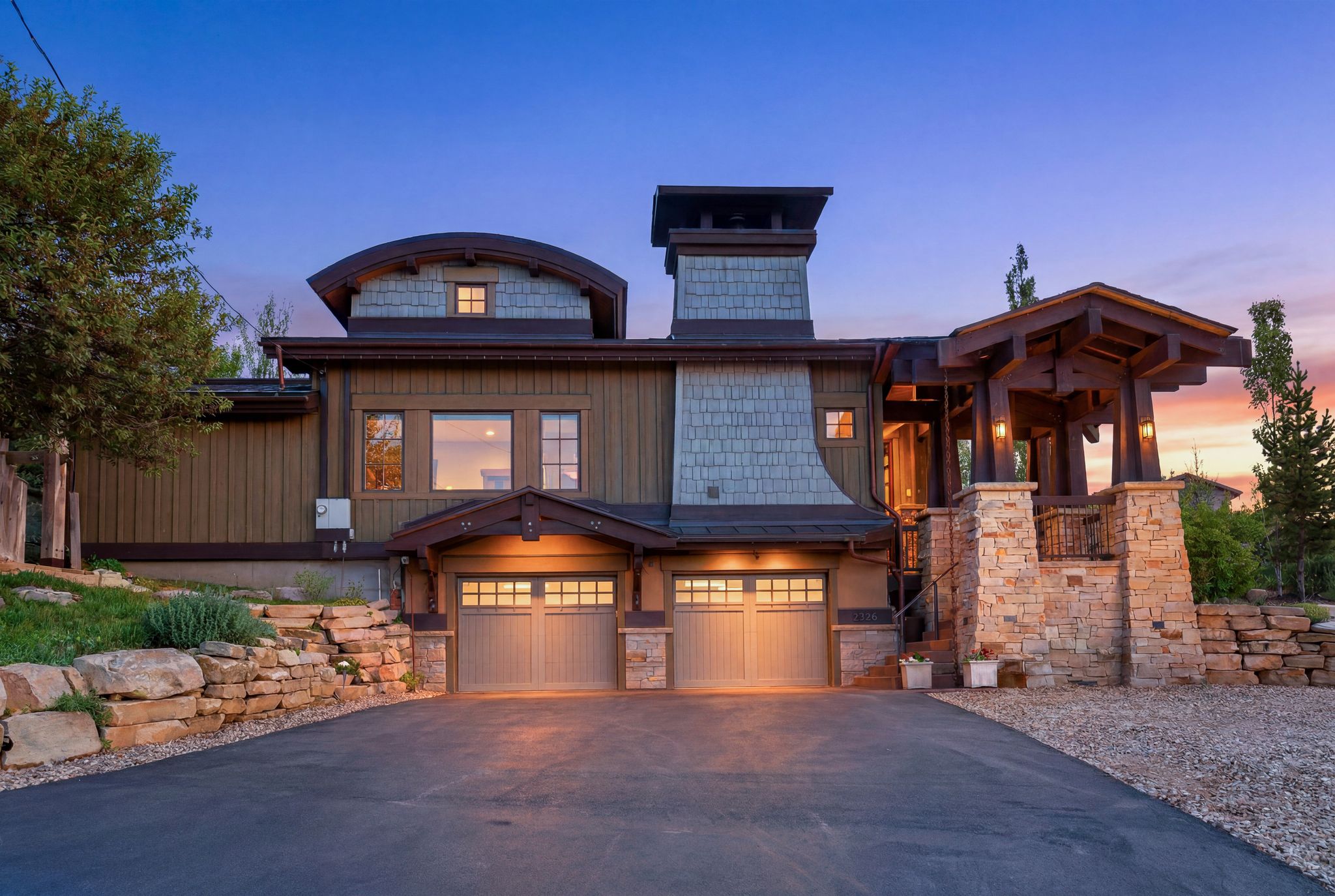 Craftsman-style exterior featuring cedar shake siding, stone accents, two attached garage bays, a covered entryway with exposed timber beams, and a paved driveway