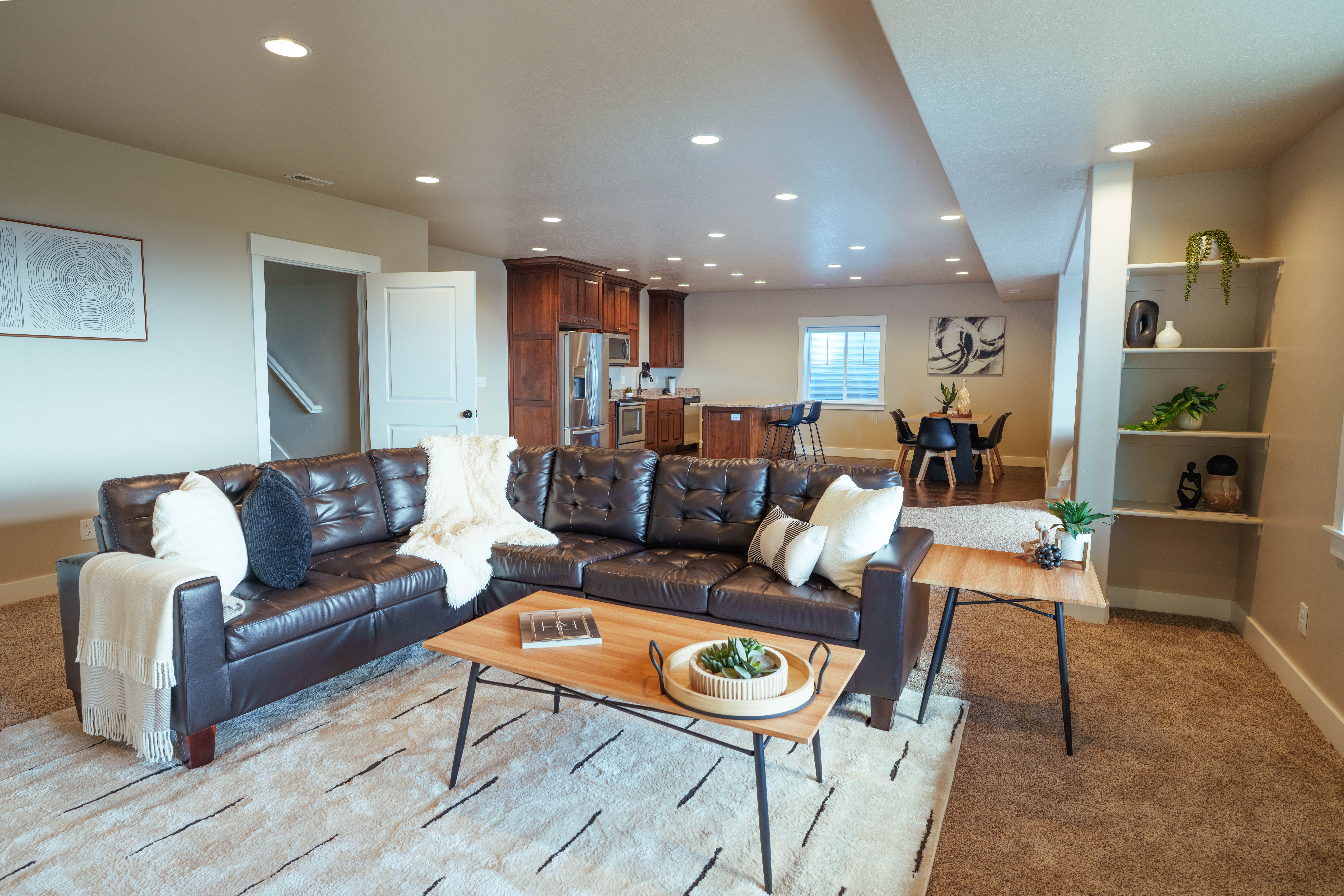 Open-concept living area featuring recessed lighting, a neutral color palette, built-in shelving, a kitchen with dark wood cabinetry, and a dining area with a window