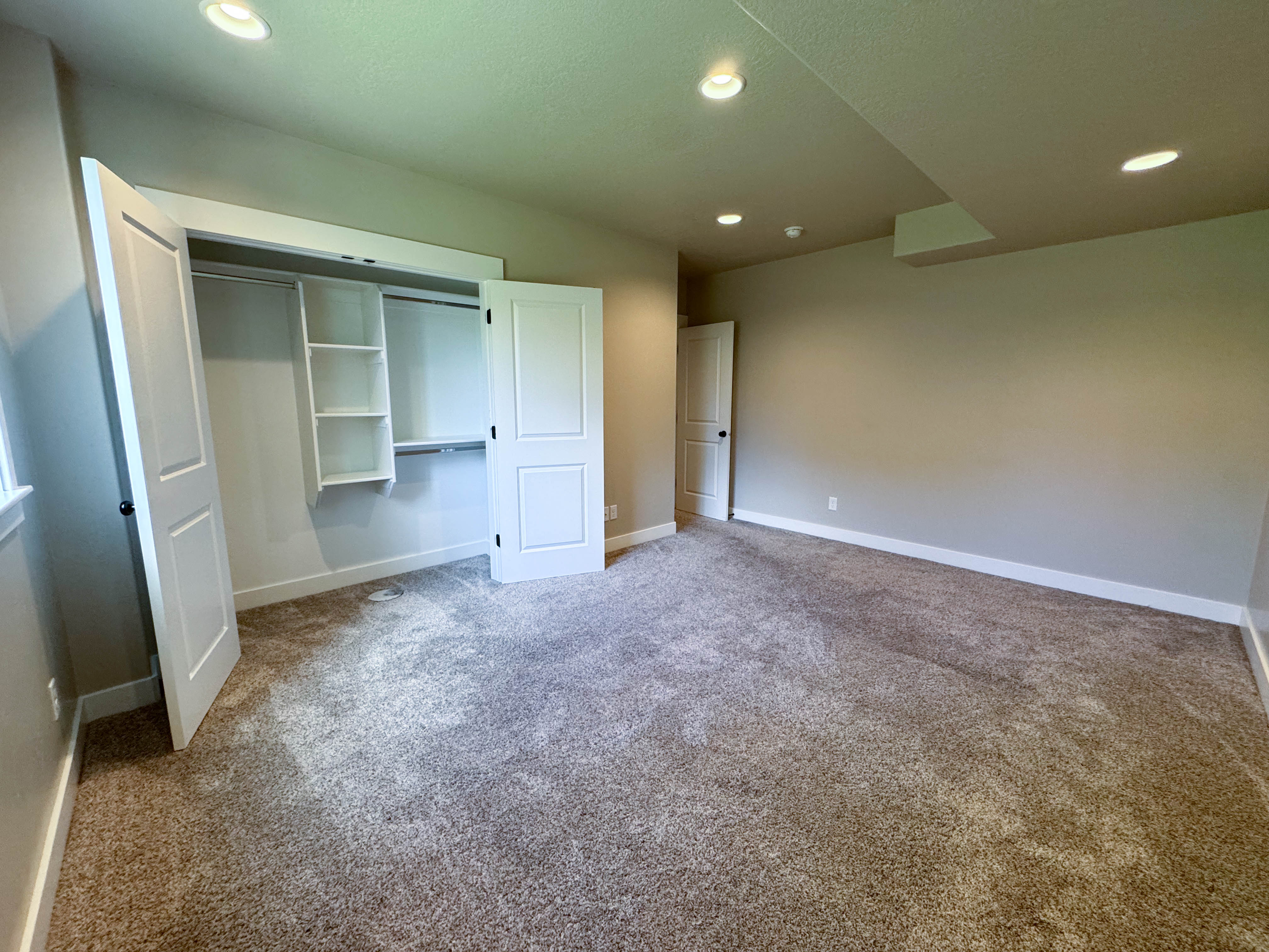 Spacious room featuring neutral carpet, recessed lighting, white baseboards, and a closet with bifold doors and built-in shelving