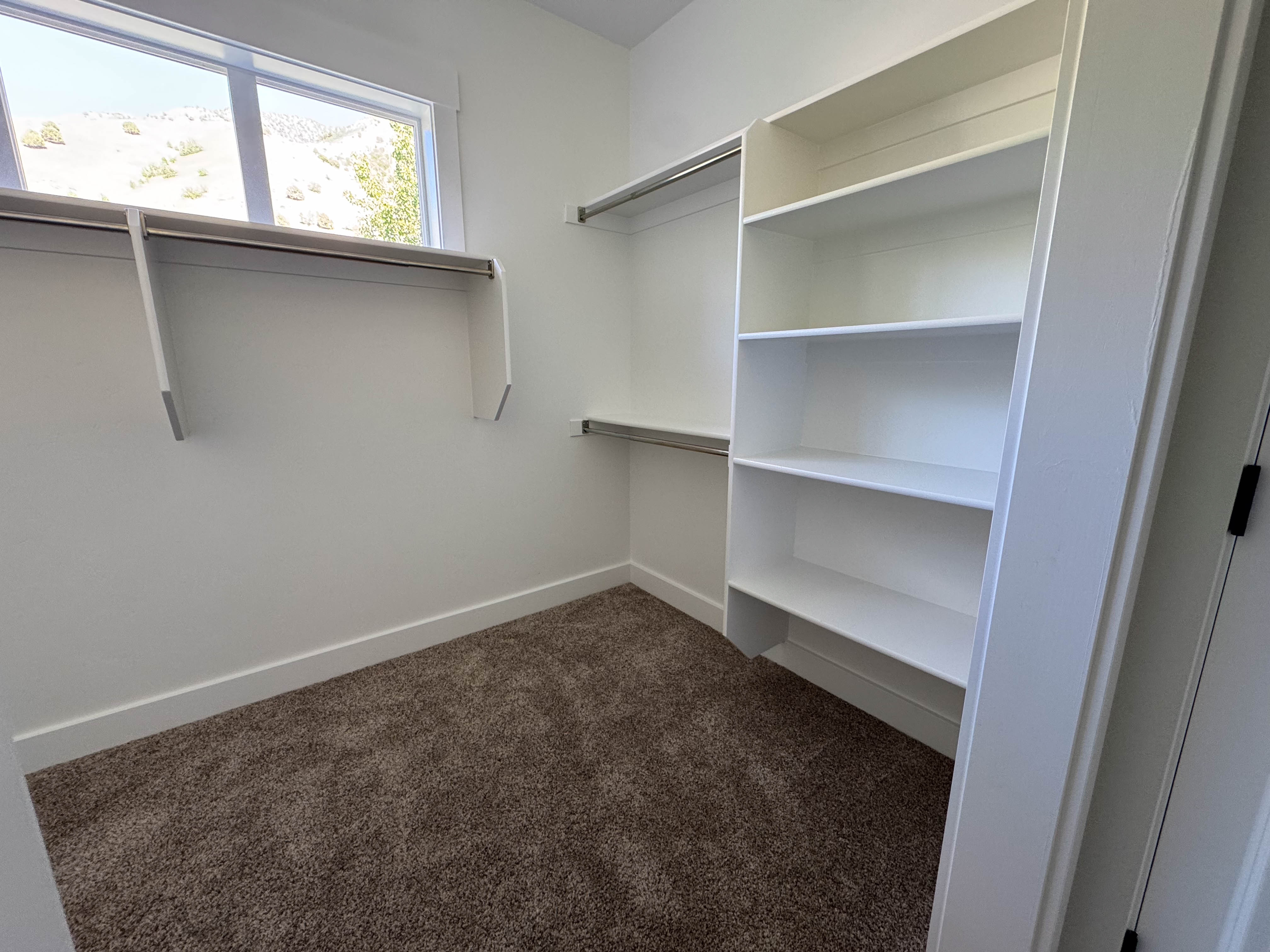 Spacious closet featuring built-in shelving, hanging rods, and a window for natural illumination