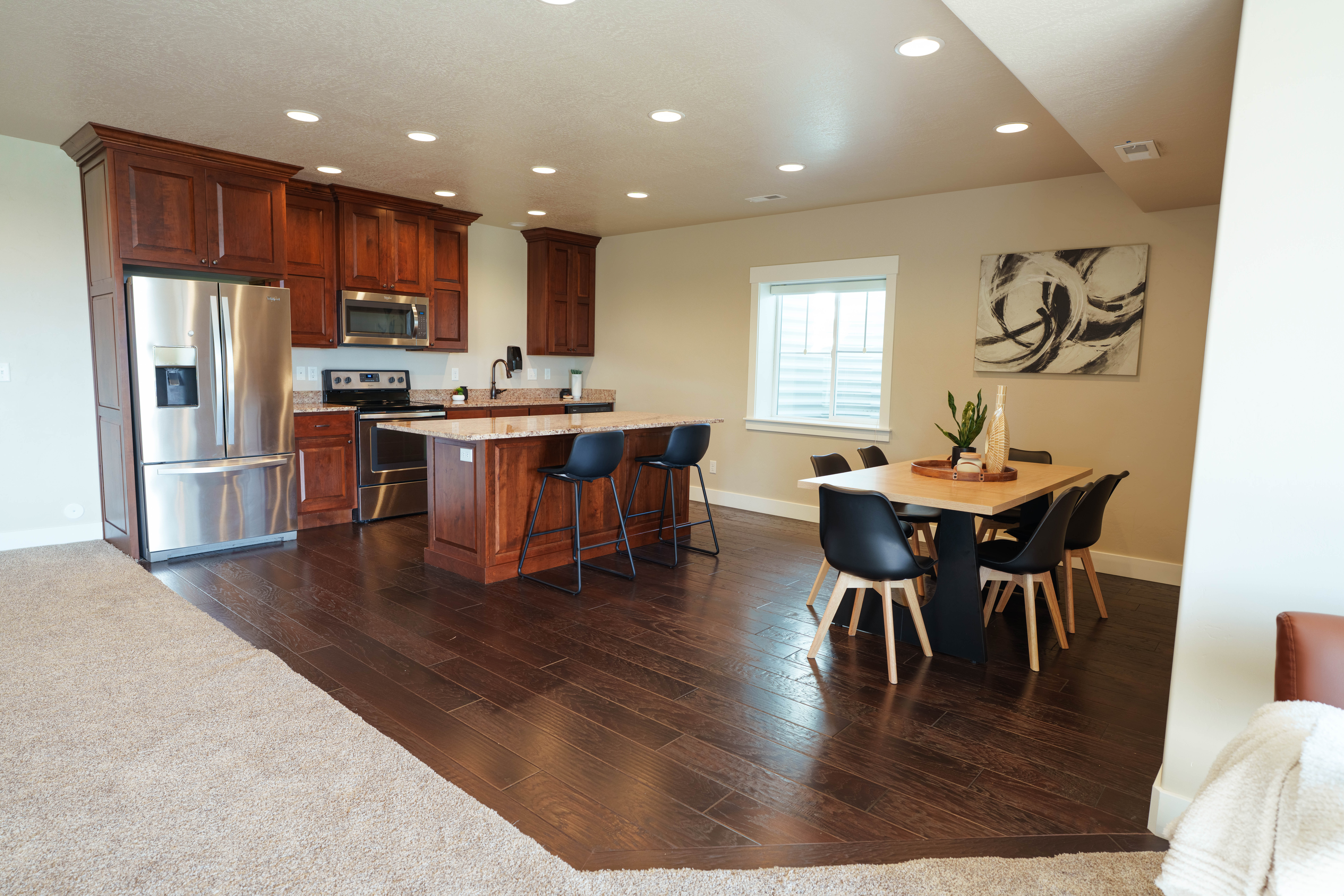 Open-concept kitchen and dining area featuring rich wood cabinetry, stainless steel appliances, a granite-topped island, wood-finish flooring, and recessed lighting