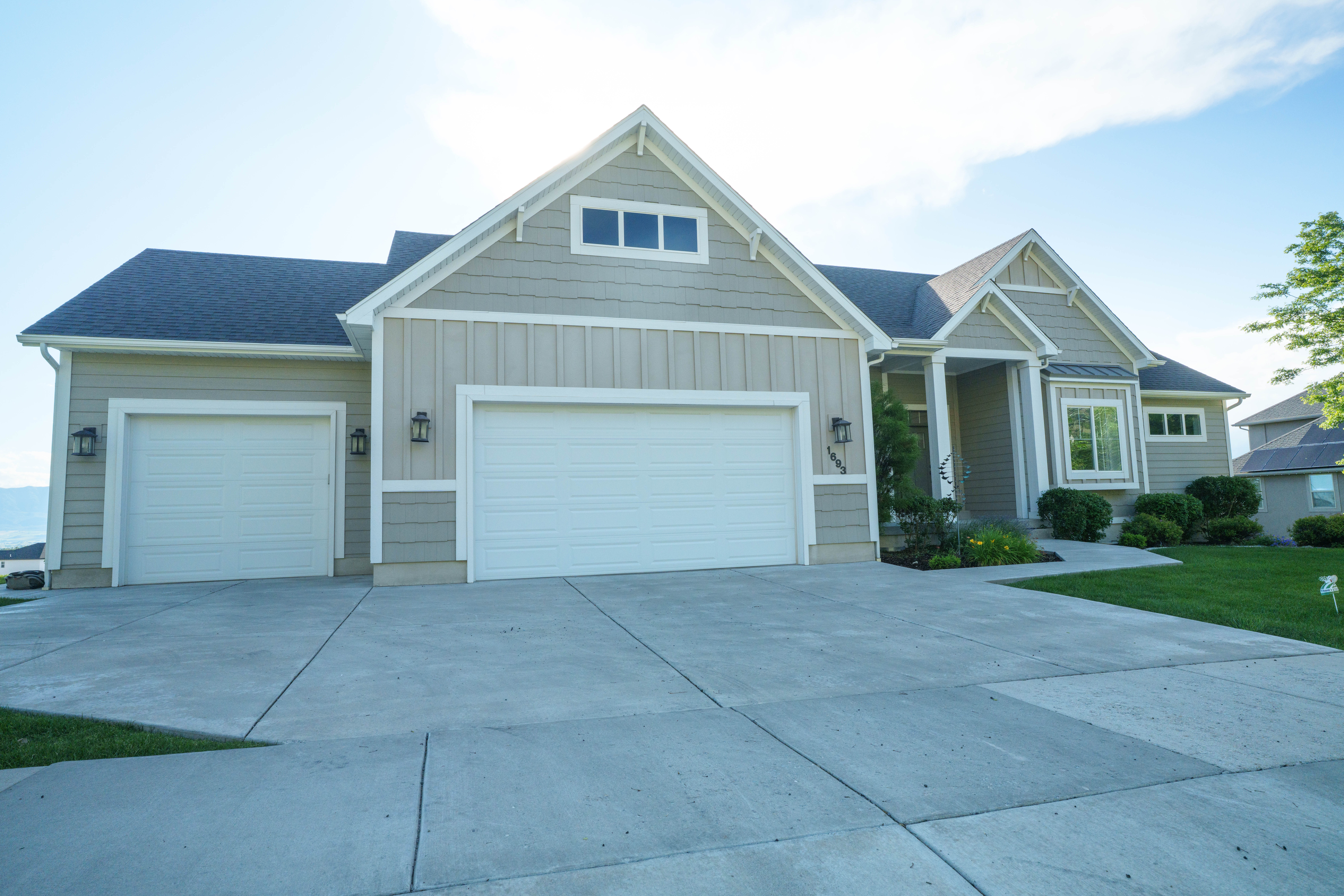 Modern Craftsman-style  exterior with a three-car garage, light tan siding, a dark roof, a bay window, and a concrete driveway