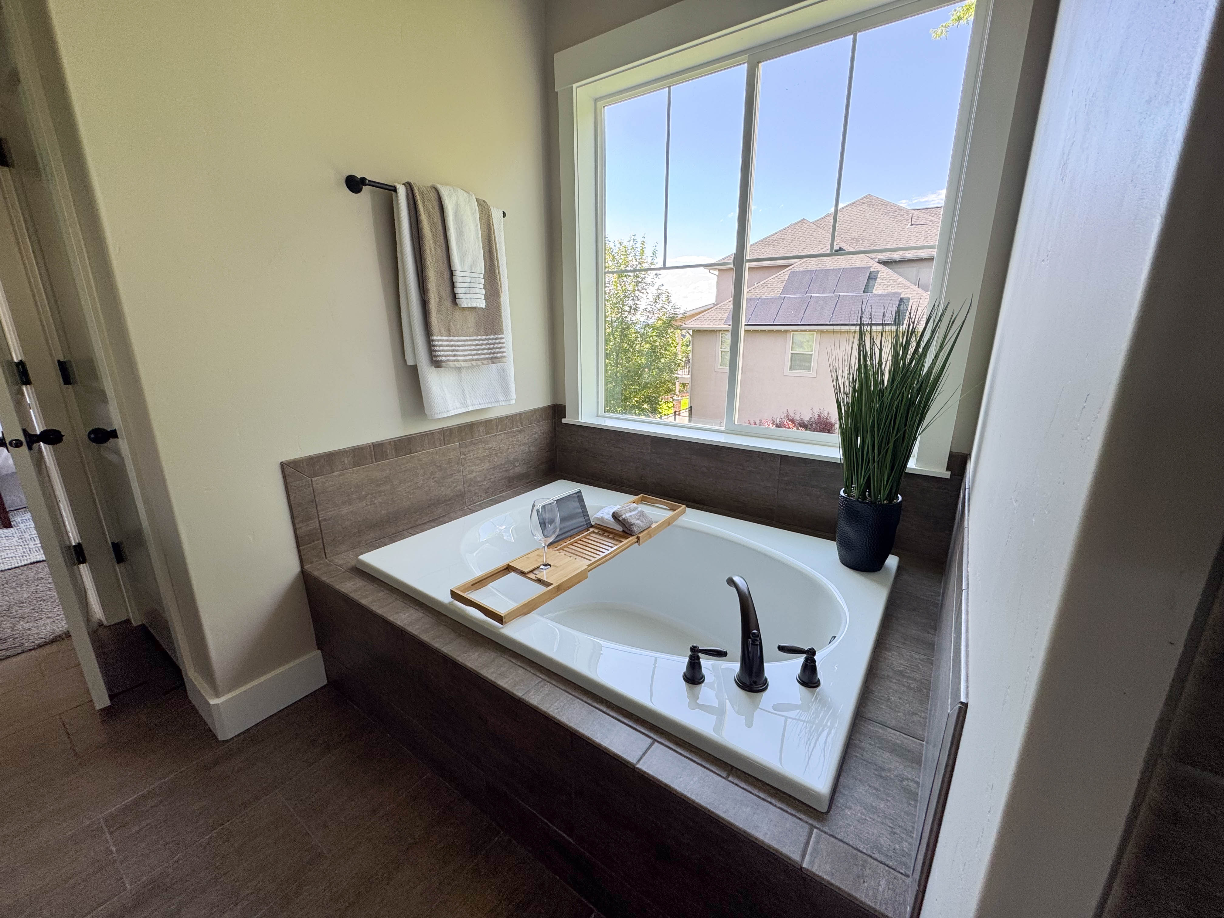 Built-in soaking tub with a dark bronze faucet, surrounded by wood-finish tile and a large window