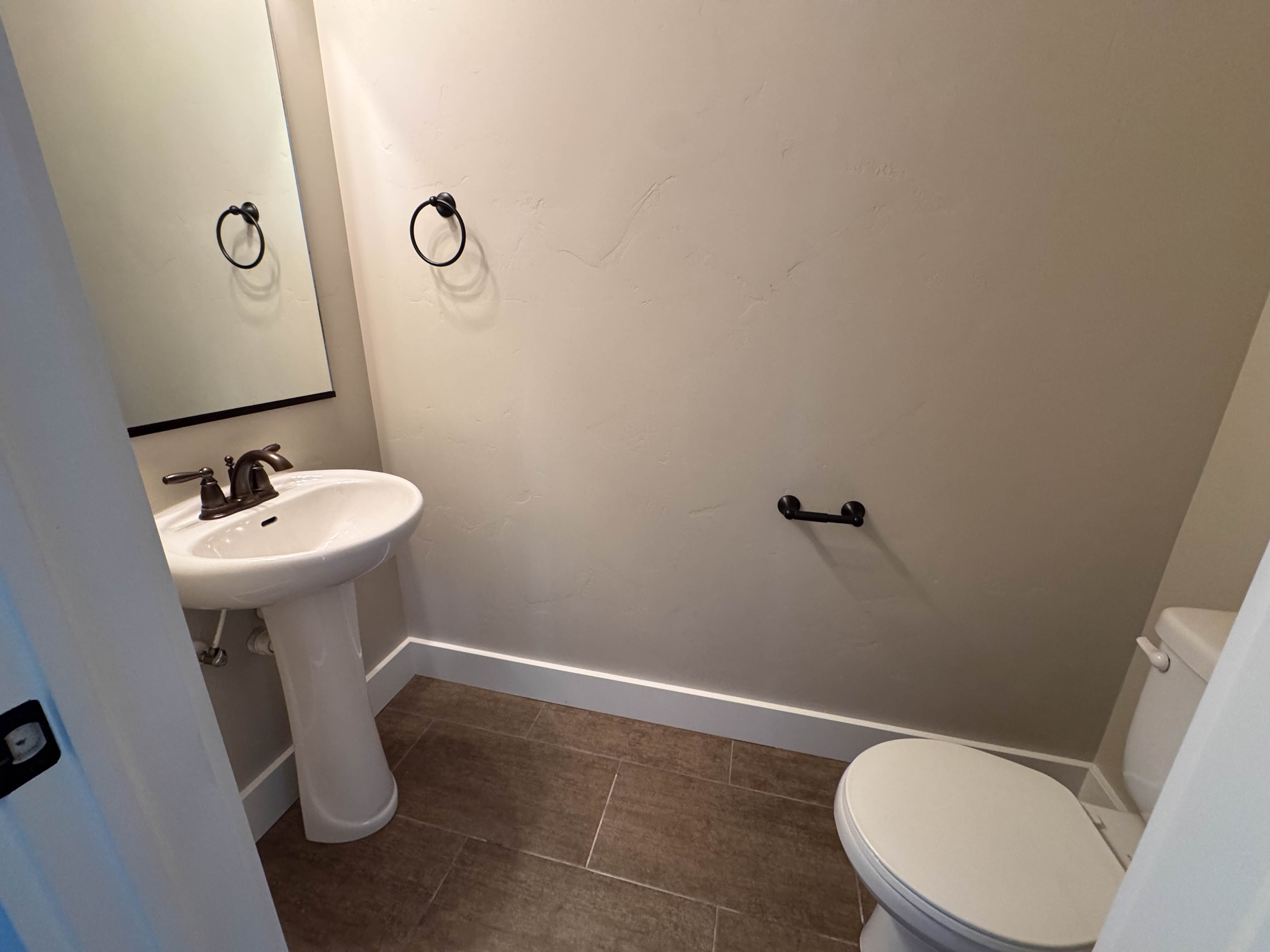 Pedestal sink with dark bronze fixtures, framed mirror, and tile flooring