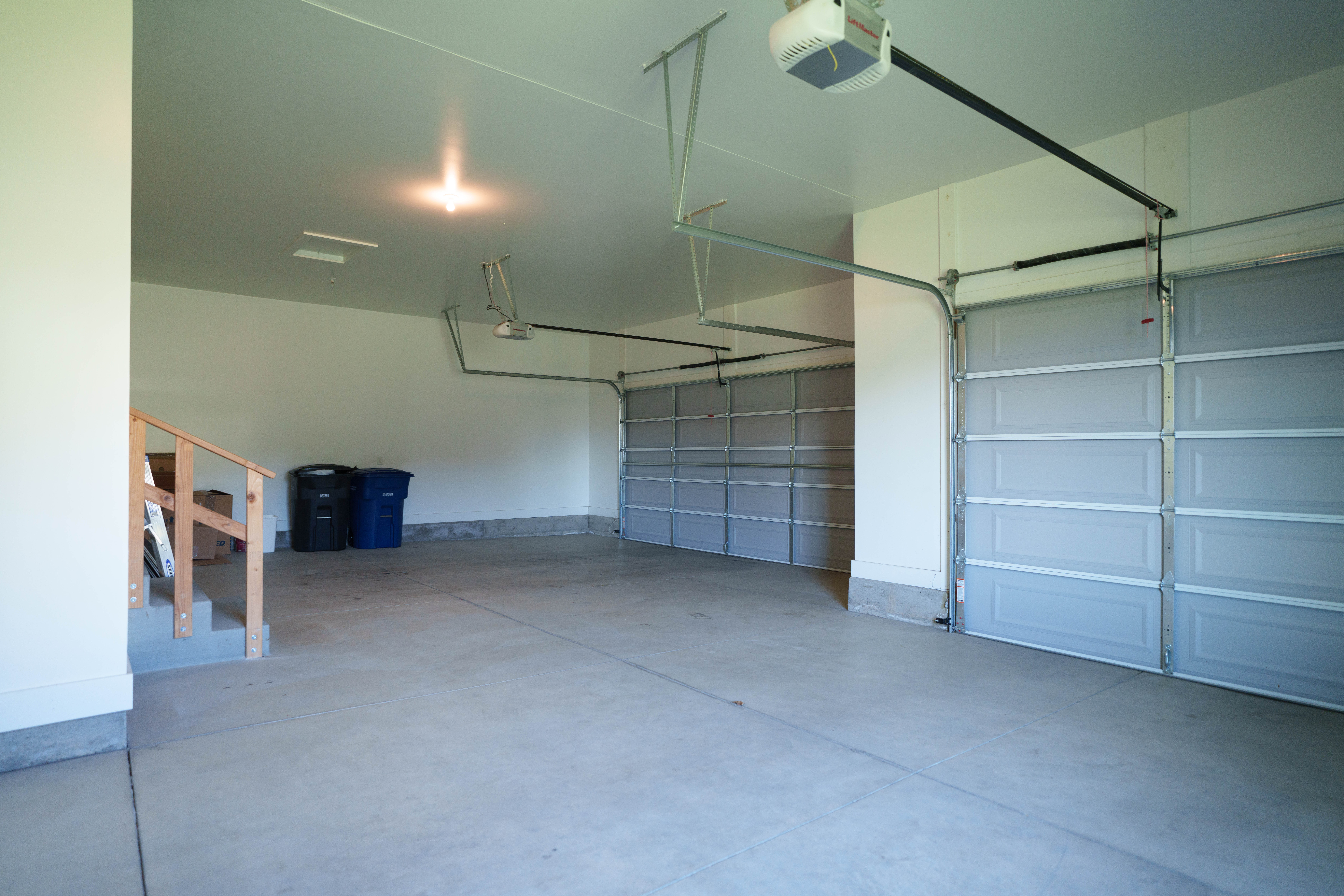 Spacious three-car garage featuring a concrete floor, light-colored walls, and automatic garage door openers